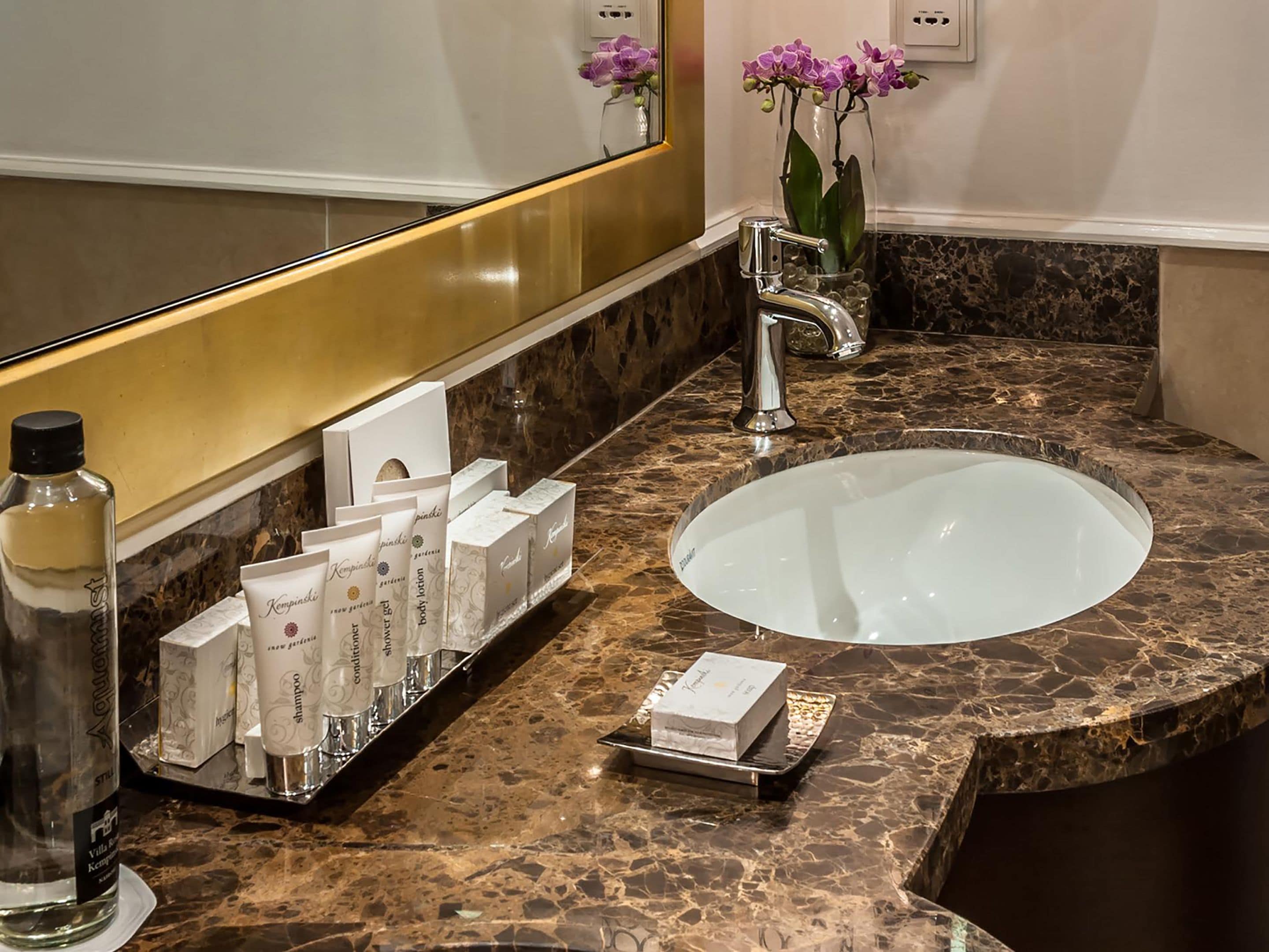 A bathroom with a marble sink, a mirror, and a tray with toiletries.