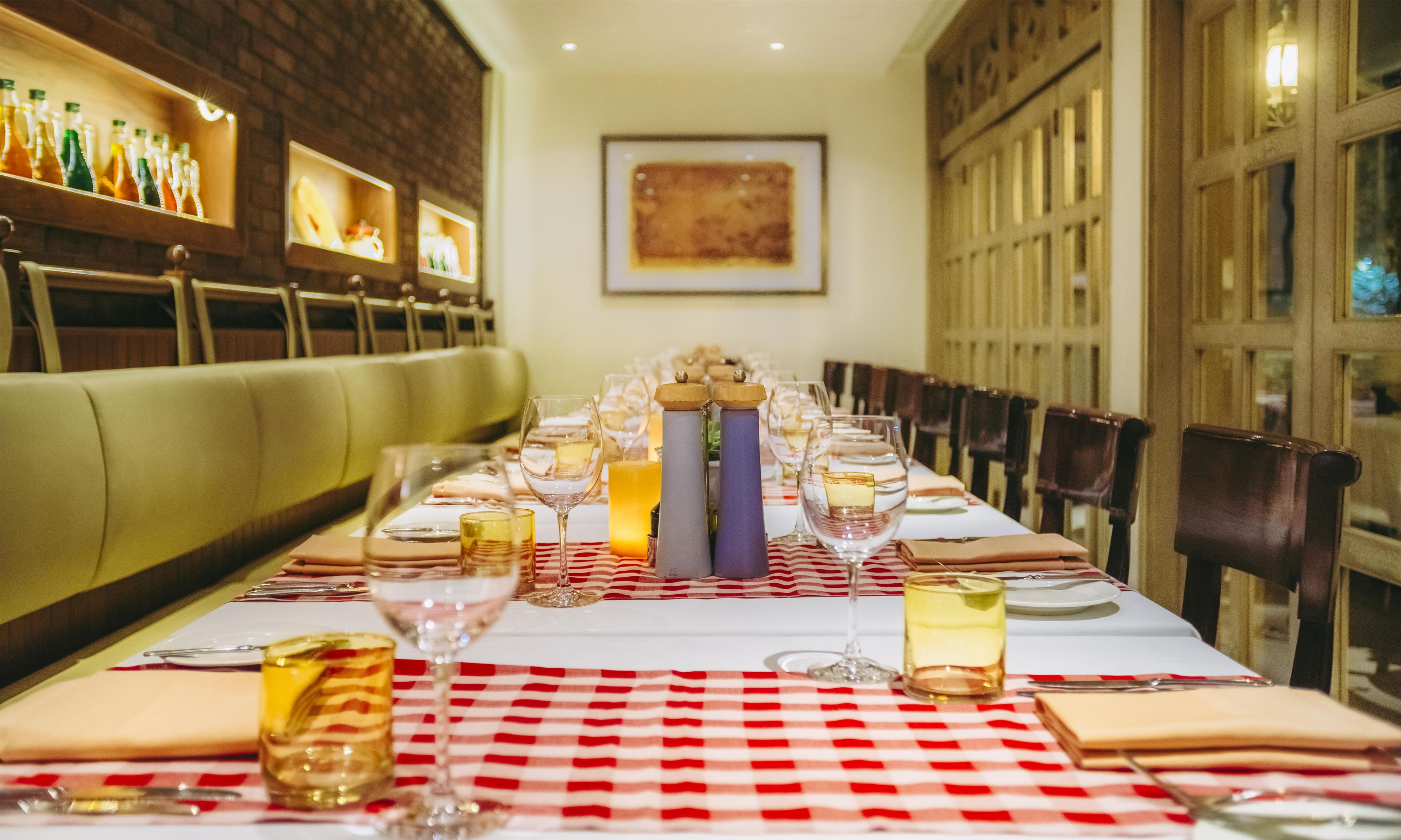 A restaurant with a long dining table set with white tablecloths, glasses, and bottles.
