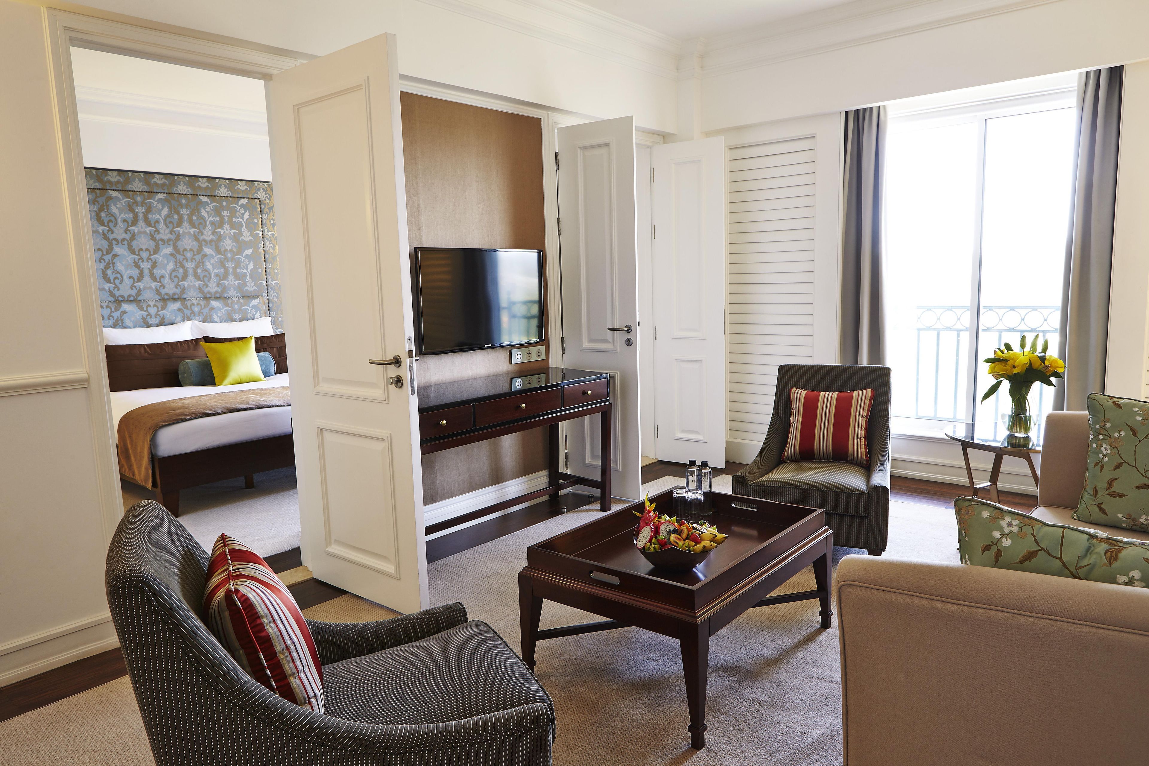 A hotel room with a bed, a TV, a dining table, and a seating area with chairs.