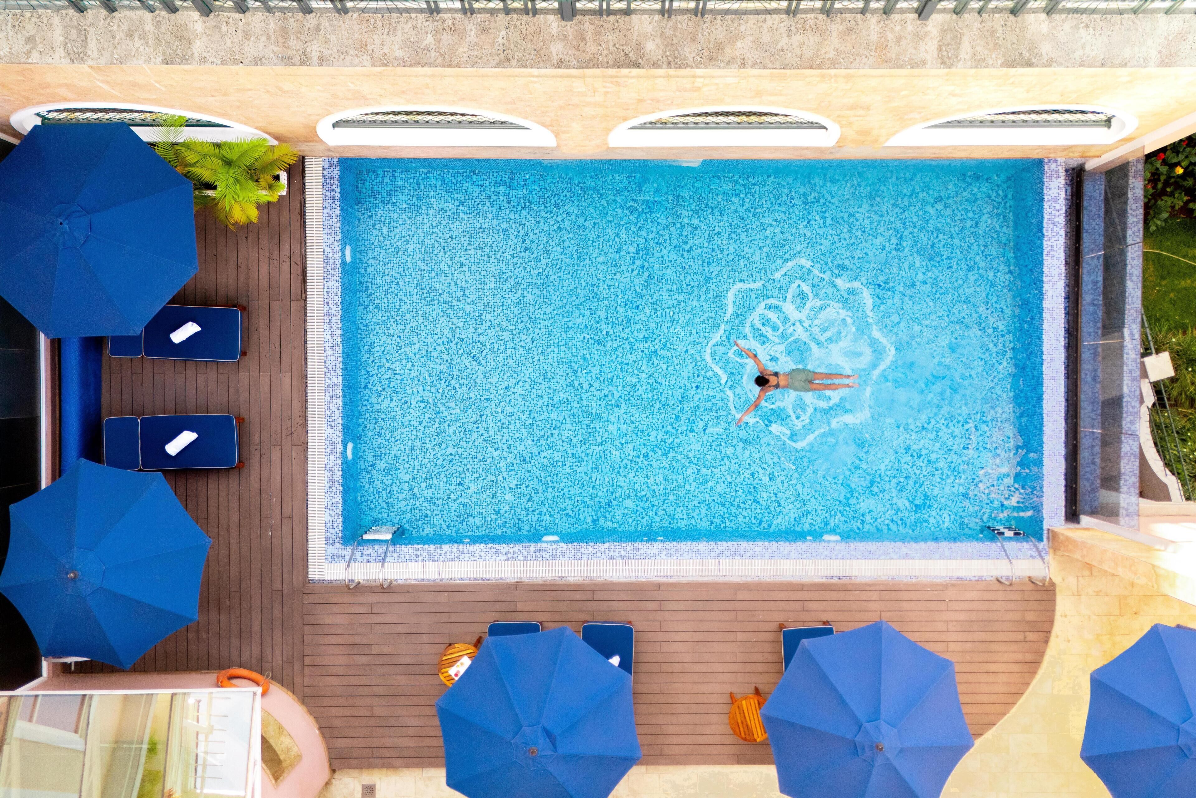 A swimming pool with a person swimming, surrounded by lounge chairs and umbrellas.