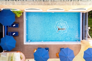 Una piscina amb una persona nedant, envoltada de gandules i ombrelles.