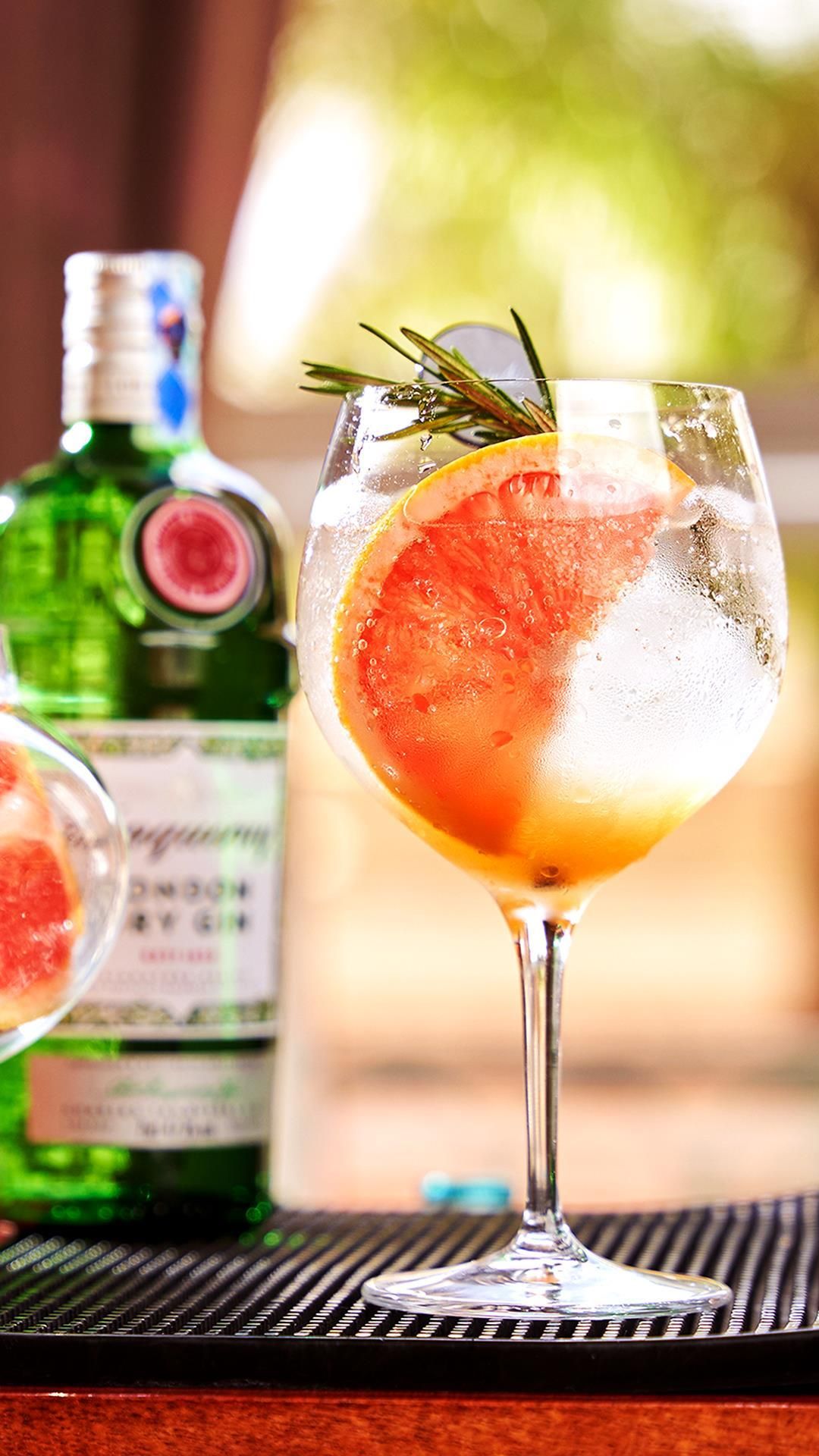 A cocktail glass with a slice of citrus fruit and a sprig of rosemary, placed on a bar mat.