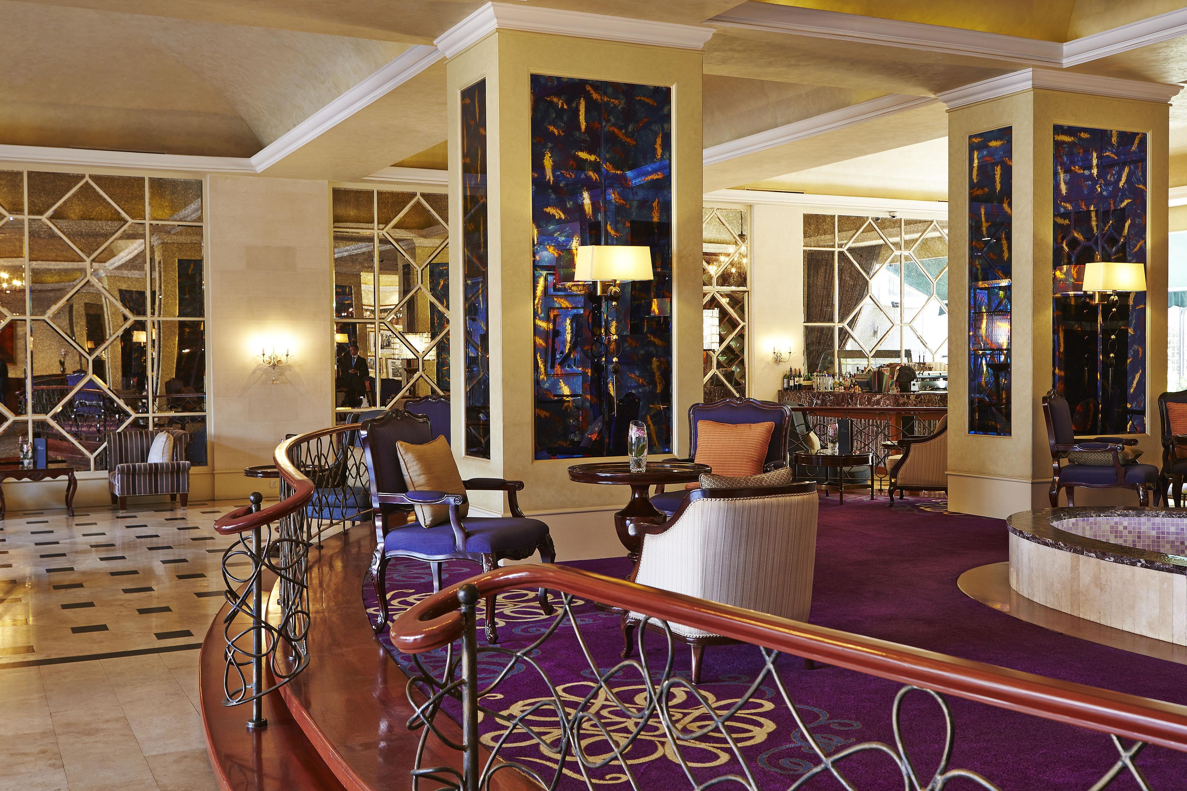 Un vestíbulo de hotel con una imponente escalera, zonas de estar y un bar.