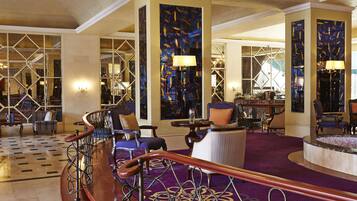 Un vestíbulo de hotel con una imponente escalera, zonas de estar y un bar.