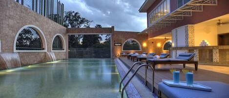 A pool area with a waterfall feature, lounge chairs, and a bar area with a tiled backsplash.