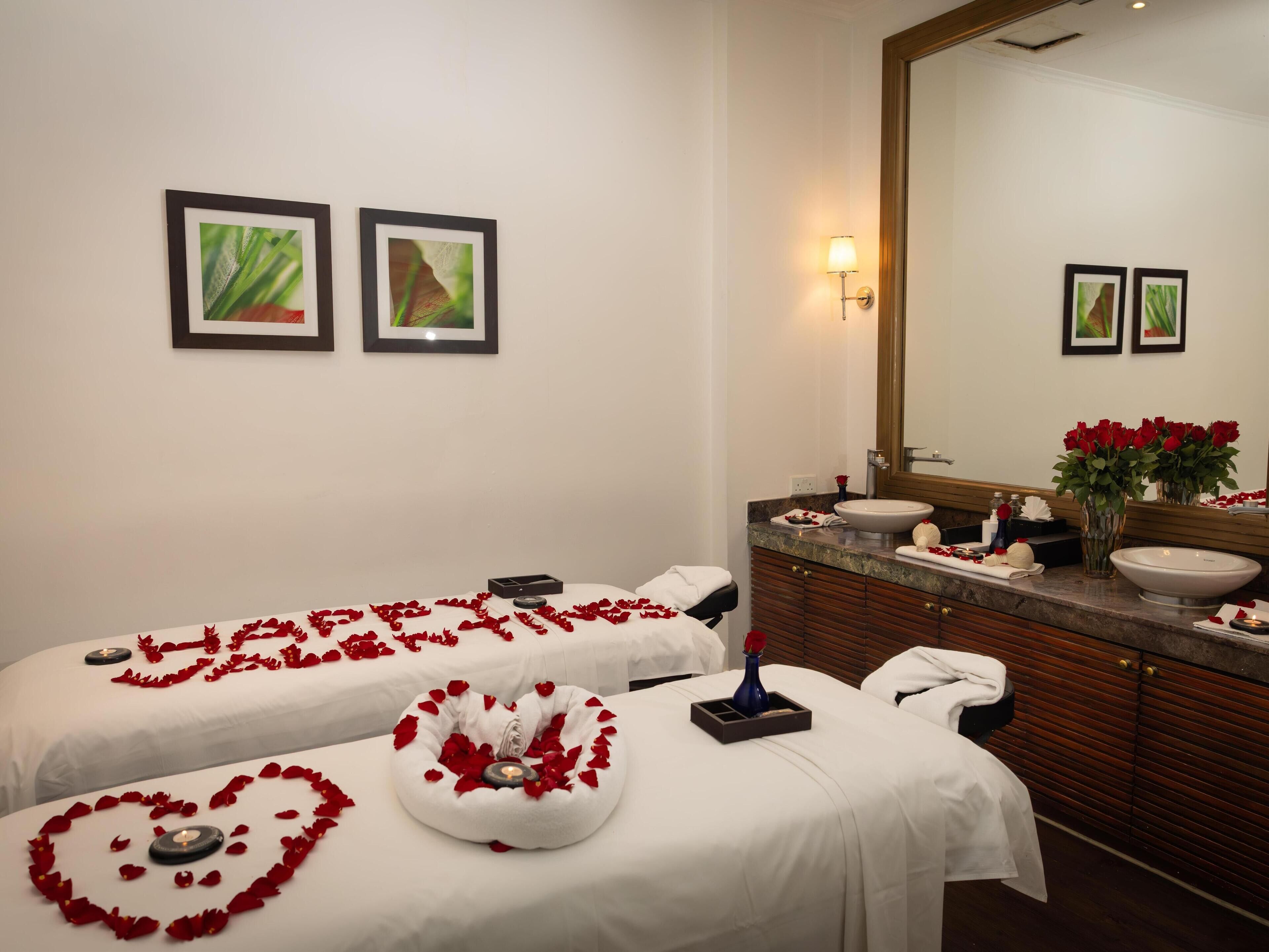 A hotel room with two massage beds, a vanity with a sink, and a mirror.