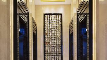A modern hallway with a patterned wall, black-framed doors, and a colorful carpet.
