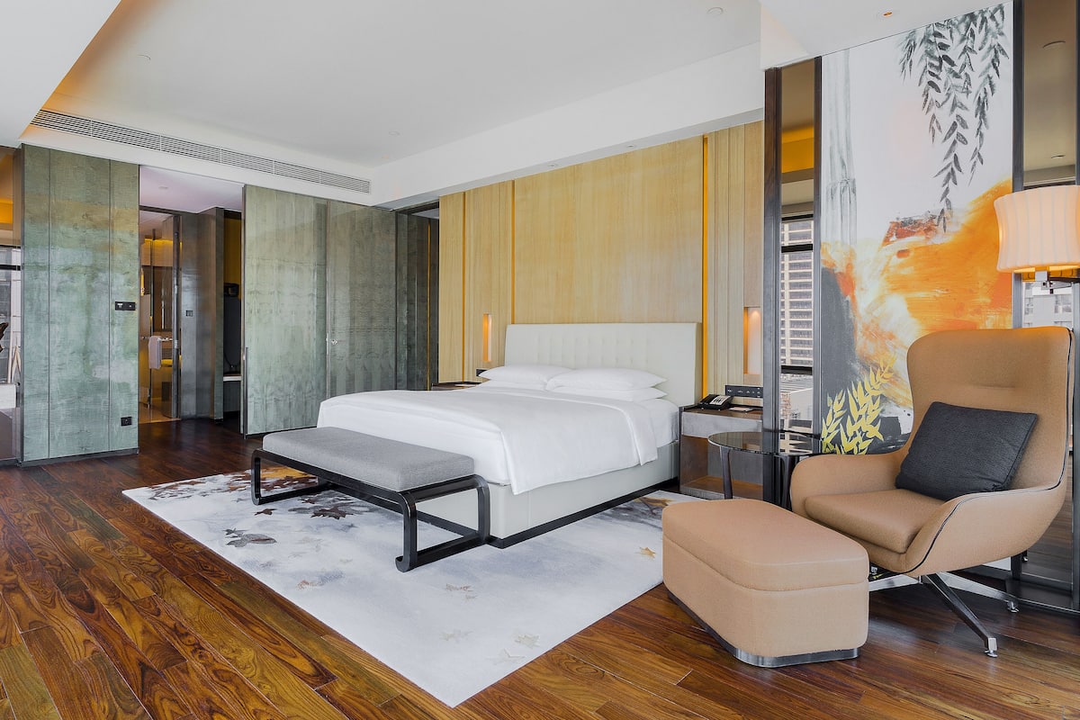 A modern hotel room with a large bed, a seating area, and a view of the city.