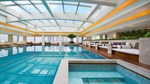 A modern indoor swimming pool with a glass ceiling, lounge areas, and a view of the city skyline. - Grand Hyatt Shenyang (Shenyang)