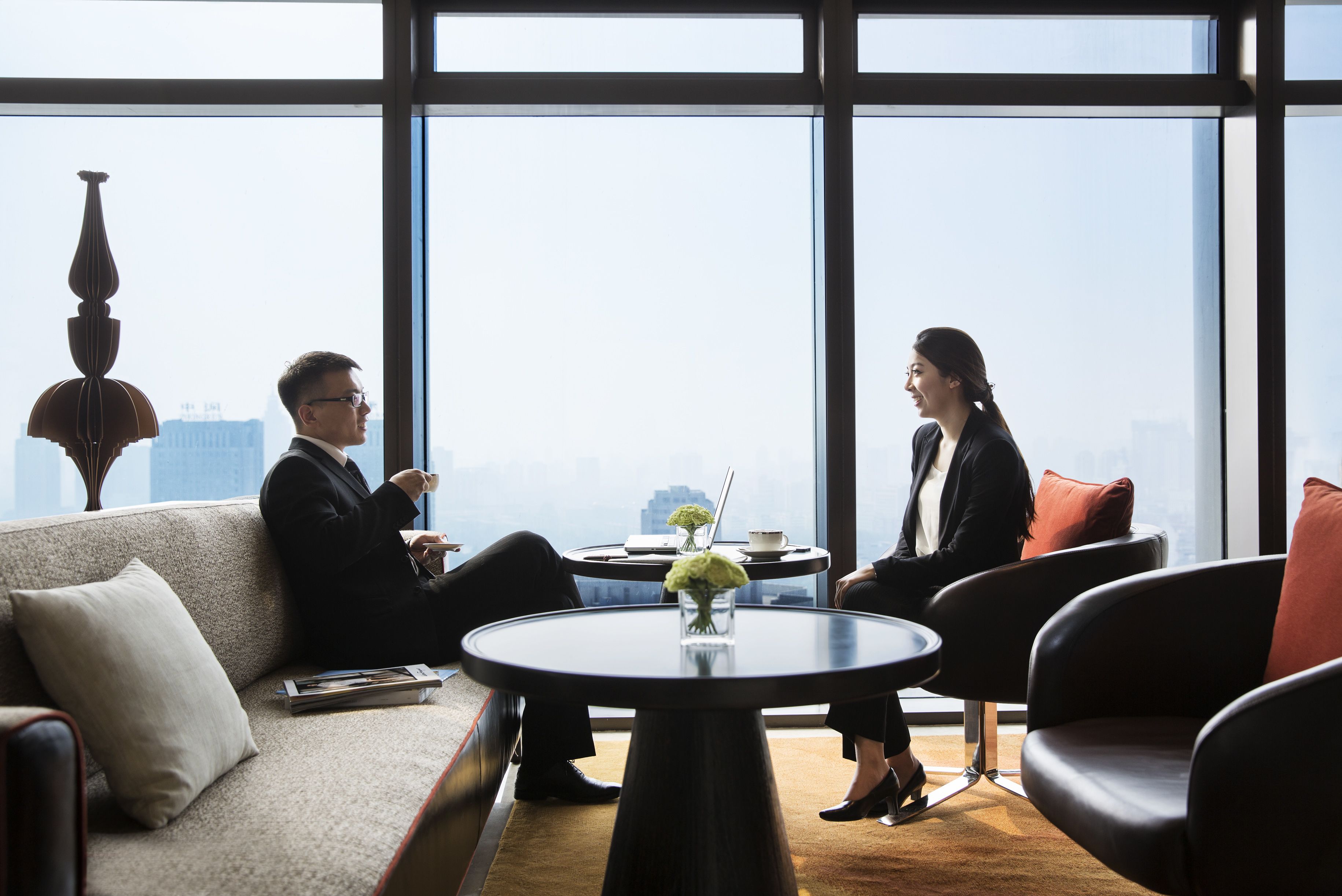 Un bureau moderne avec deux personnes assises autour d’une table ronde, un canapé et une grande fenêtre donnant sur la ville.