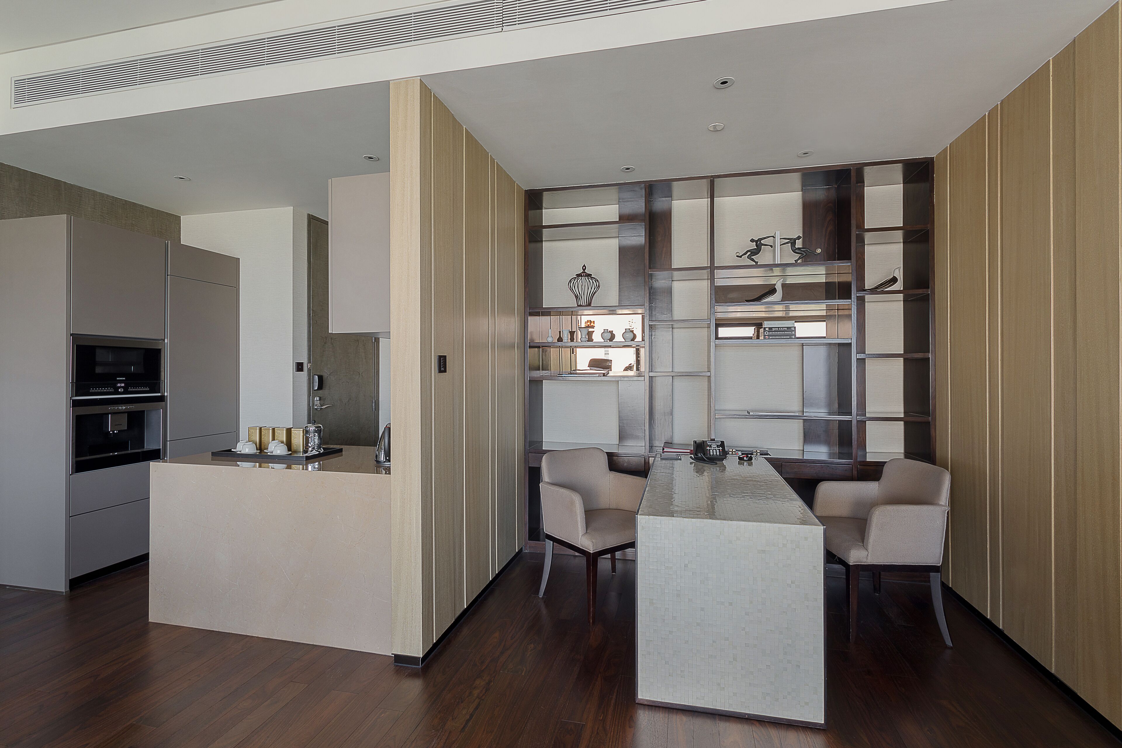 A modern kitchen with a central island, built-in appliances, and a seating area with chairs.