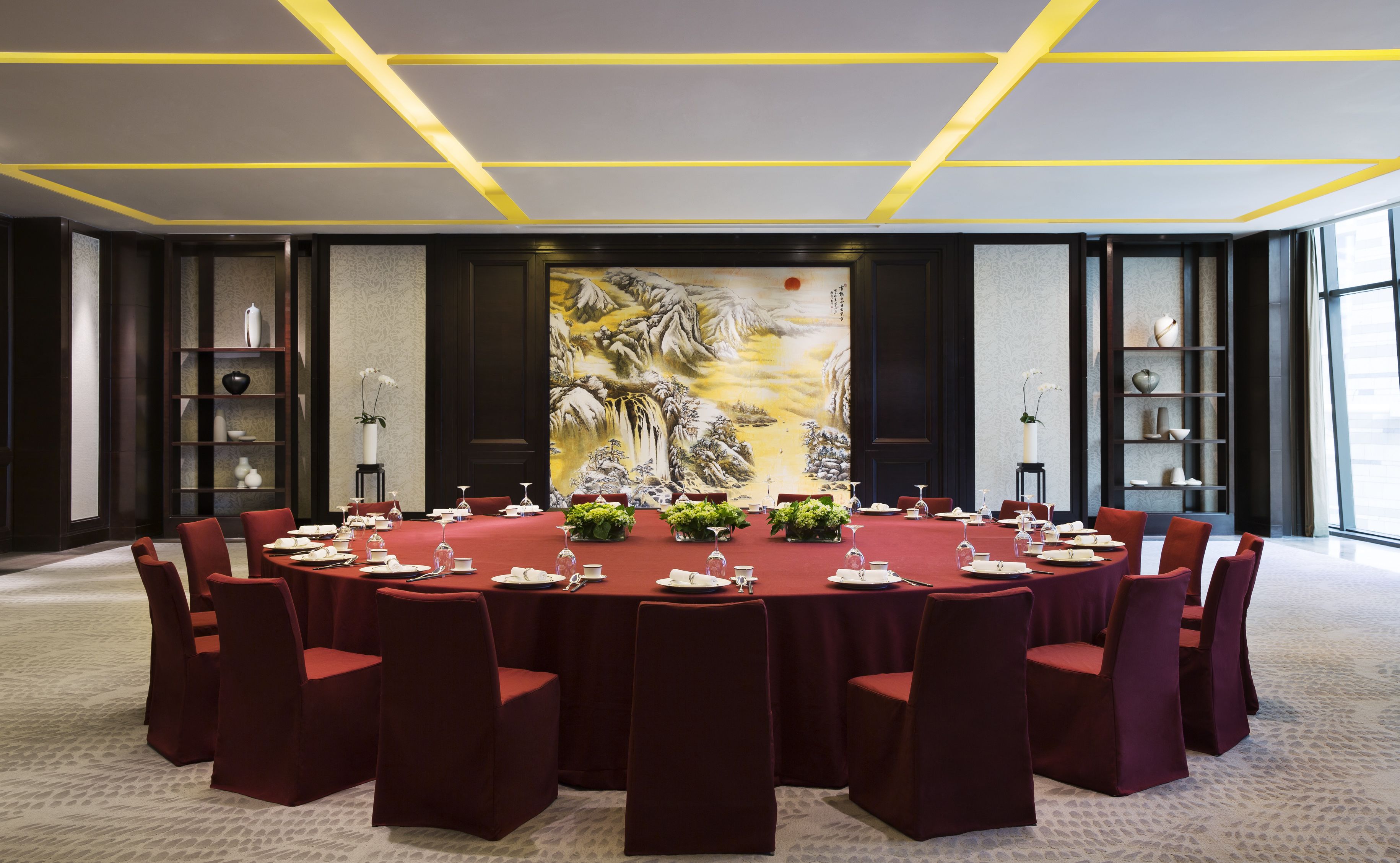 A conference room with a round table, red chairs, and a large painting on the wall.