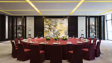 A conference room with a round table, red chairs, and a large painting on the wall.