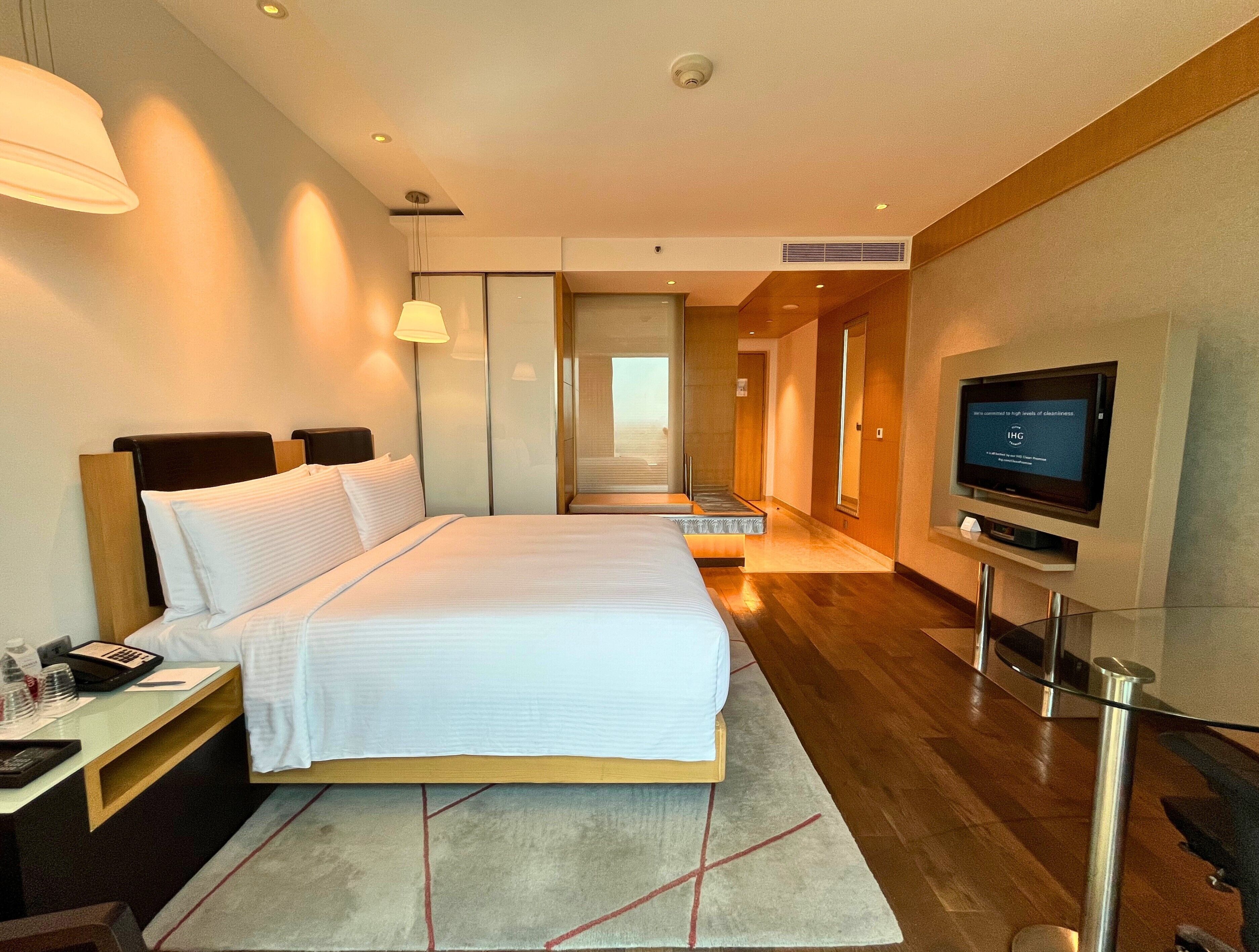 A modern hotel room with a large bed, bedside tables, a TV, and a view of the hallway.