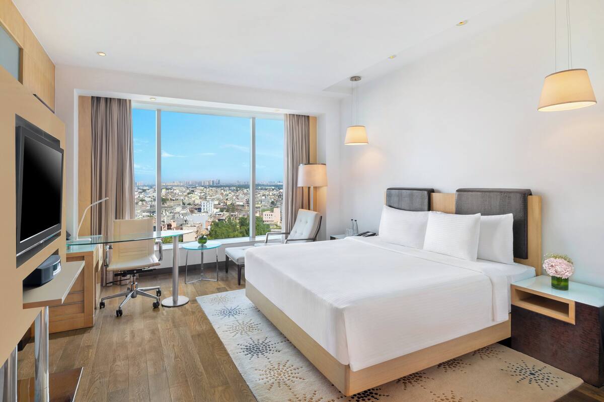Una habitación de hotel moderna con una cama grande, un escritorio con una computadora, un televisor y vistas a la ciudad.