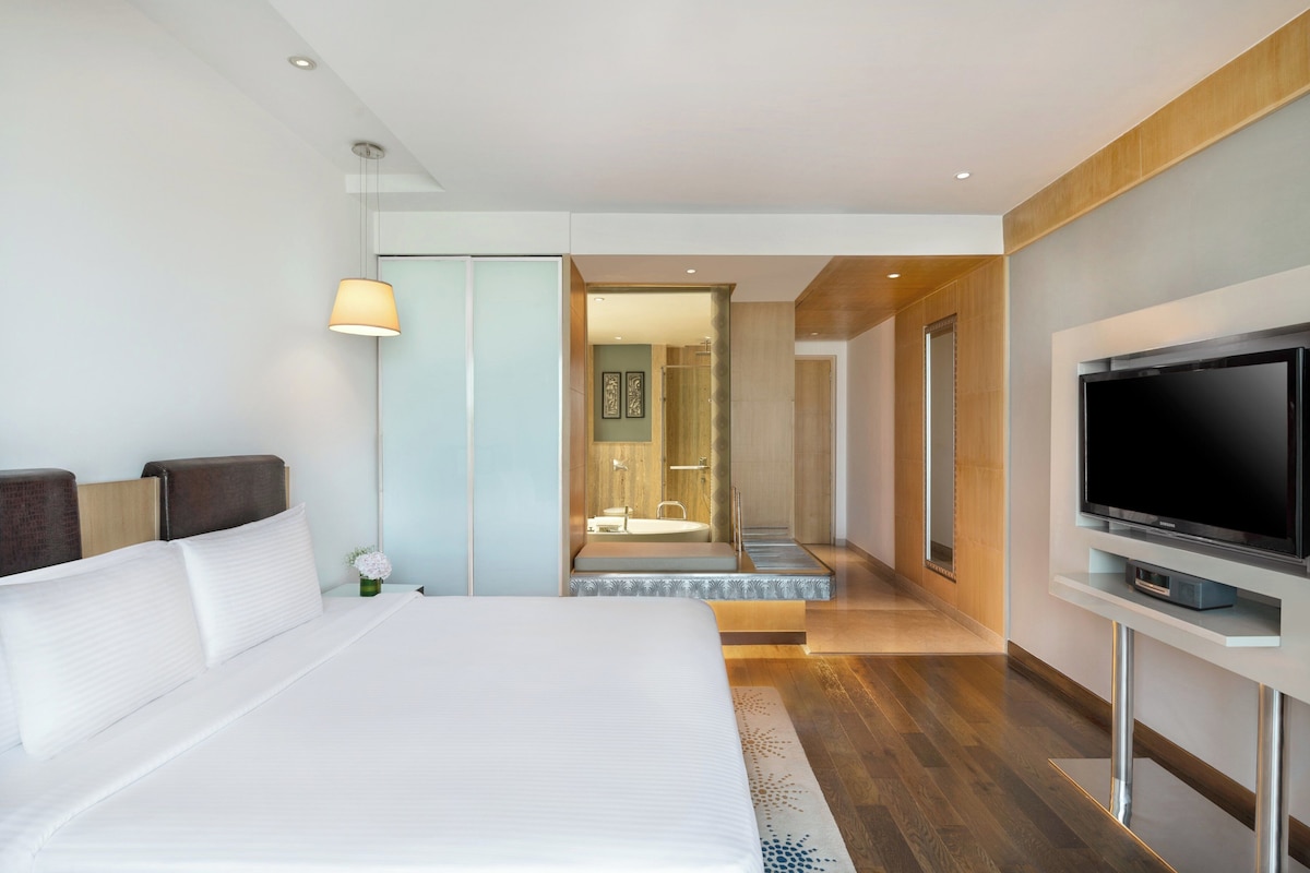 A modern hotel room with a large bed, a television, and a bathroom visible through an open door.