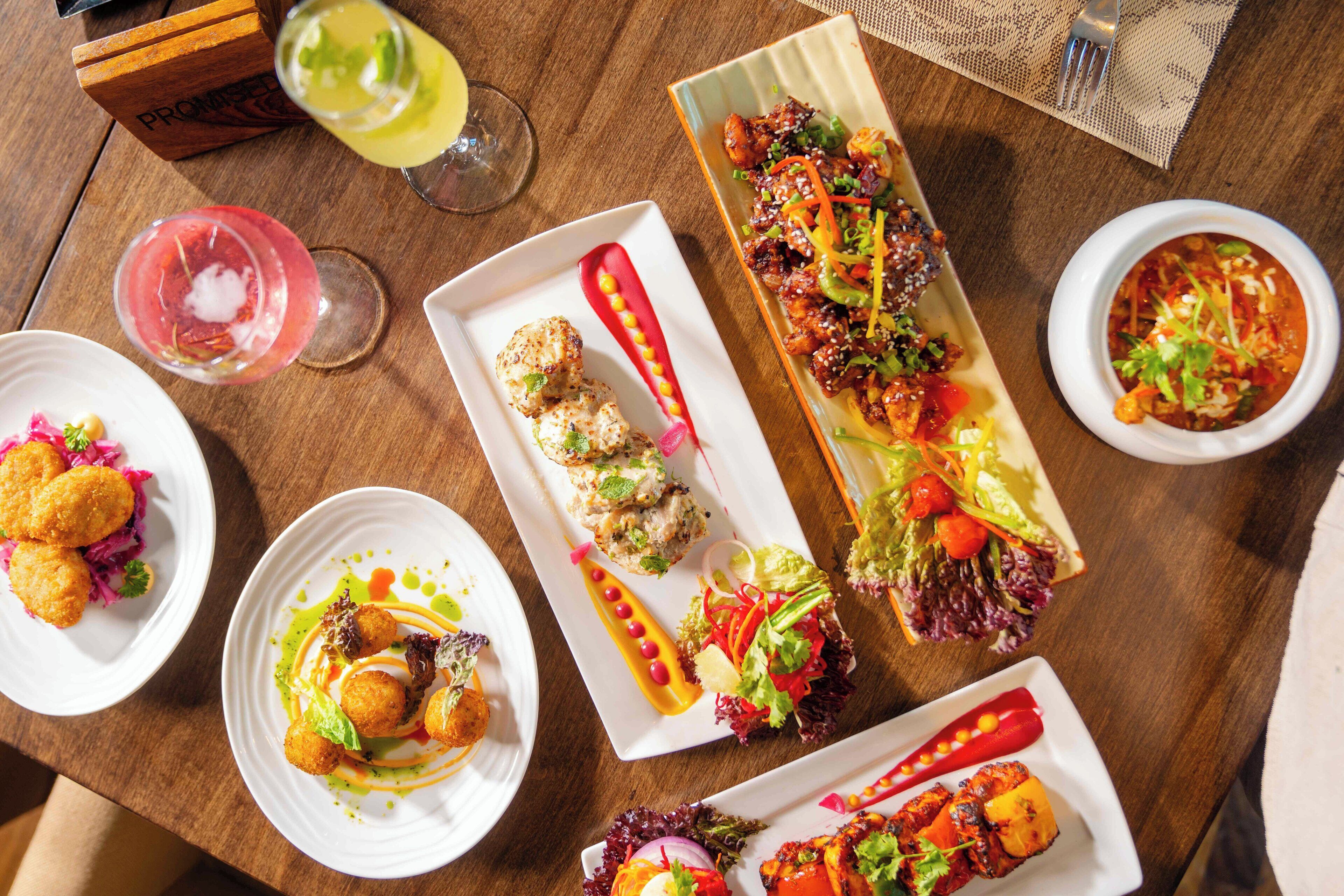 A variety of dishes on a wooden table, including grilled meats, salads, and appetizers.