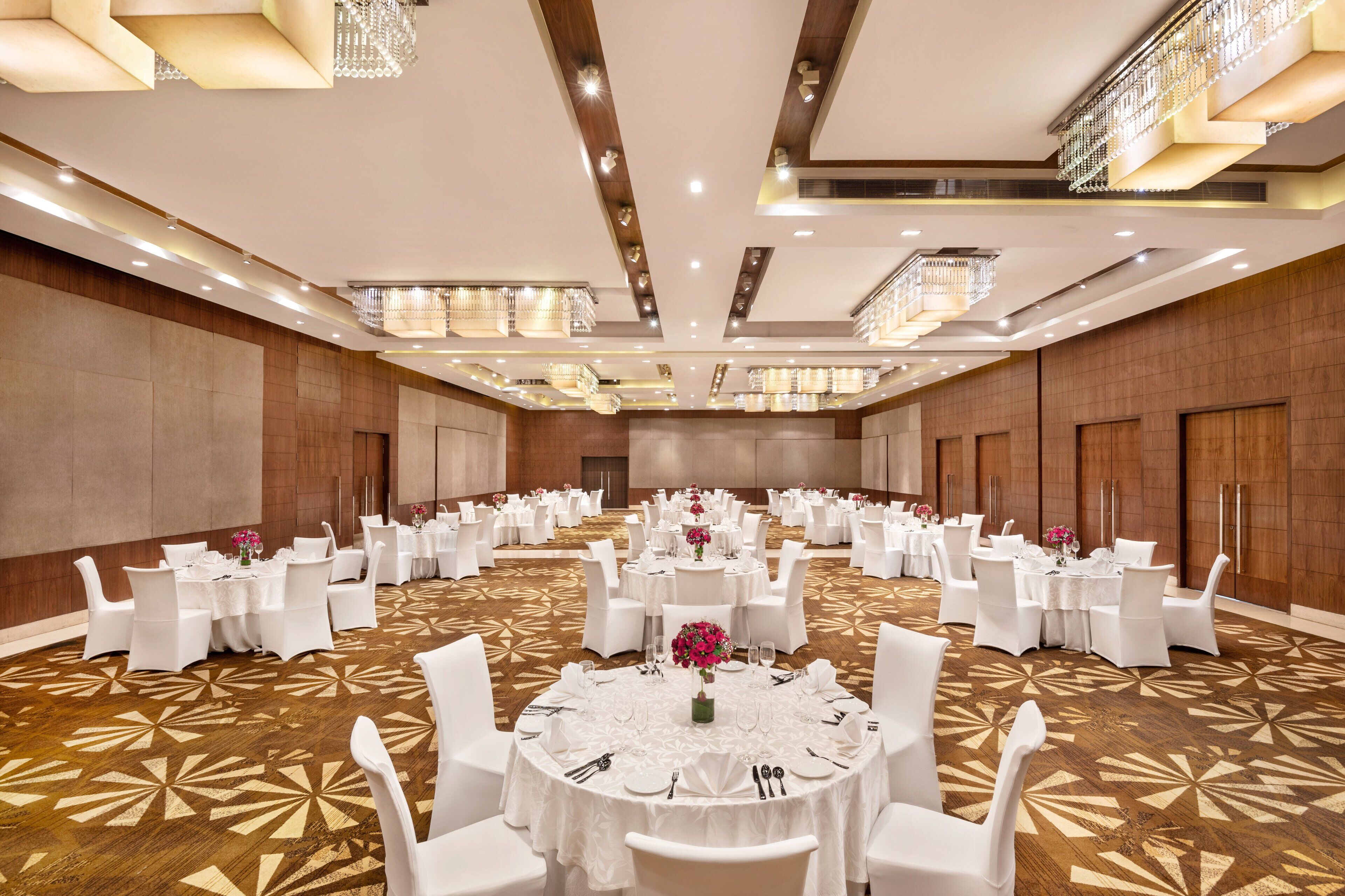 Un amplio salón de banquetes con mesas redondas, sillas blancas y candelabros.