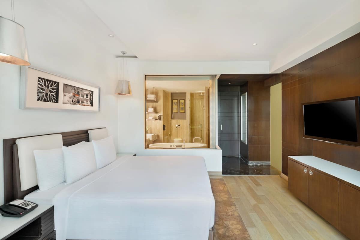 Una habitación de hotel con una cama grande, un televisor, un escritorio con teléfono y un baño visible a través de una puerta abierta.