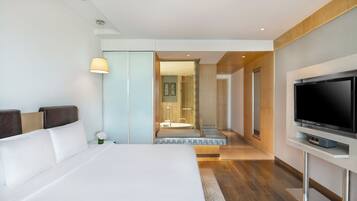 Una habitación de hotel moderna con una cama grande, un televisor de pantalla plana y un baño visible a través de una puerta abierta.