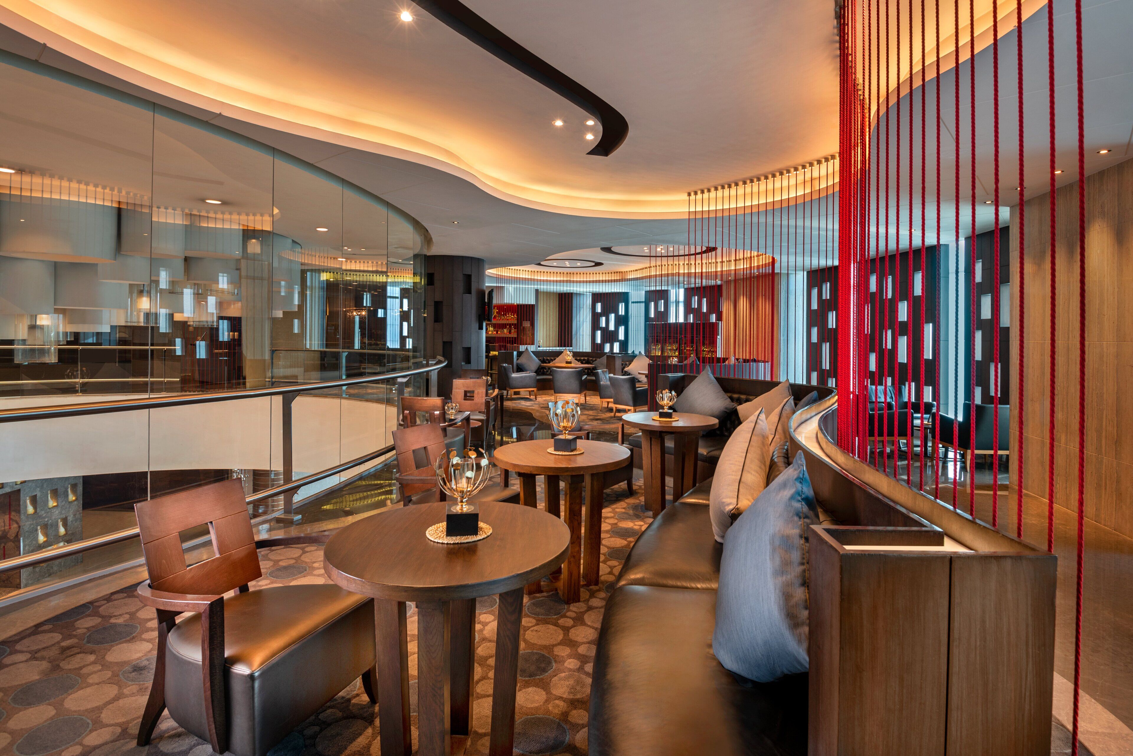 A modern lounge area with seating, tables, and a glass railing overlooking a lower level.