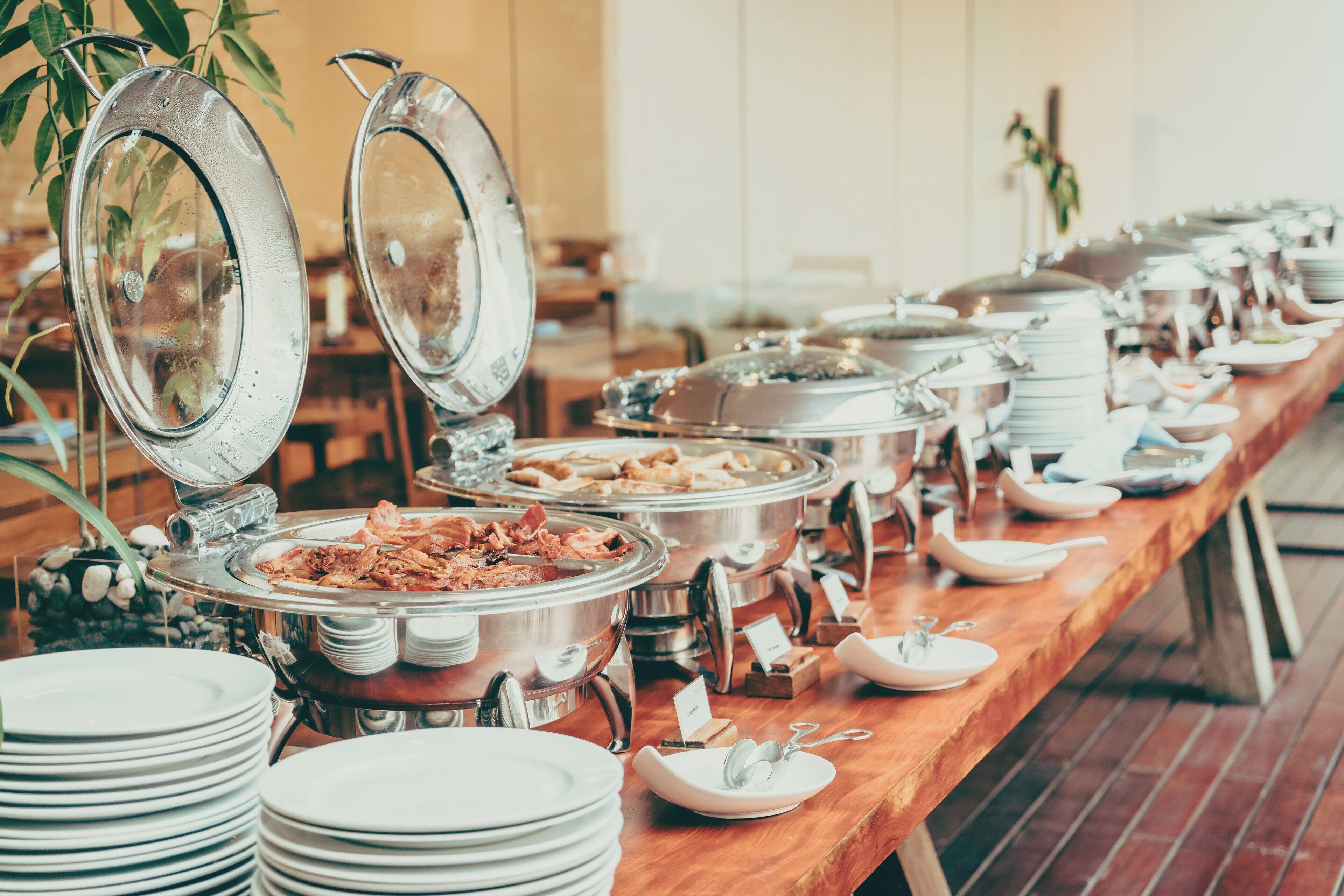 A buffet setup with multiple food stations and stacked white plates.