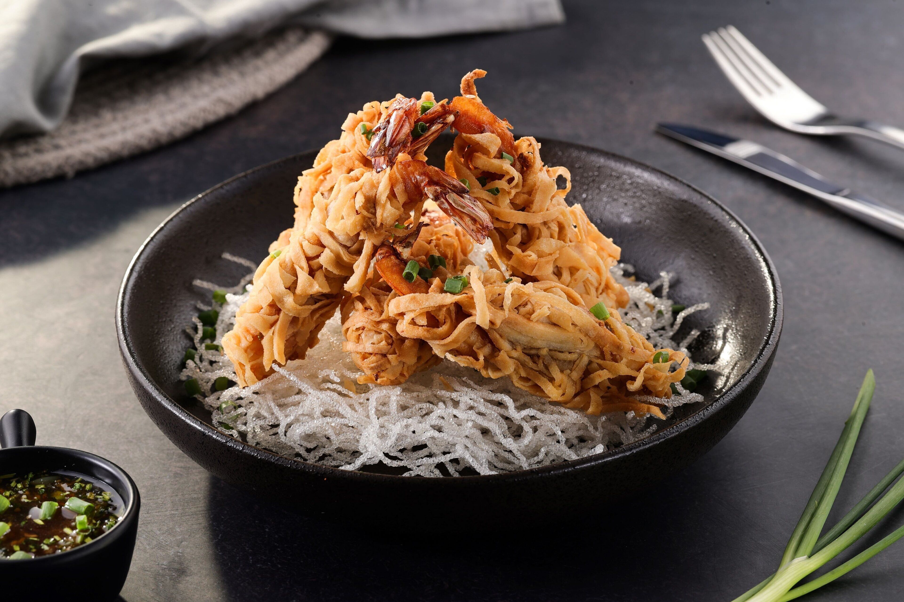 Una ciotola di noodles con gamberi e cipollotto su un piatto.