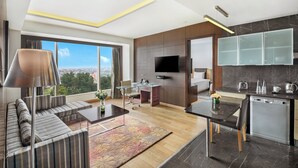 Una sala de estar moderna con sofá, una mesa de centro y televisor. Se observa una cocina con lavavajillas y armarios.