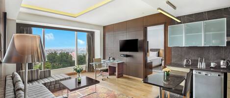 Een moderne hotelkamer met een groot raam, een bank, een eethoek, een keuken en een flatscreen-televisie.