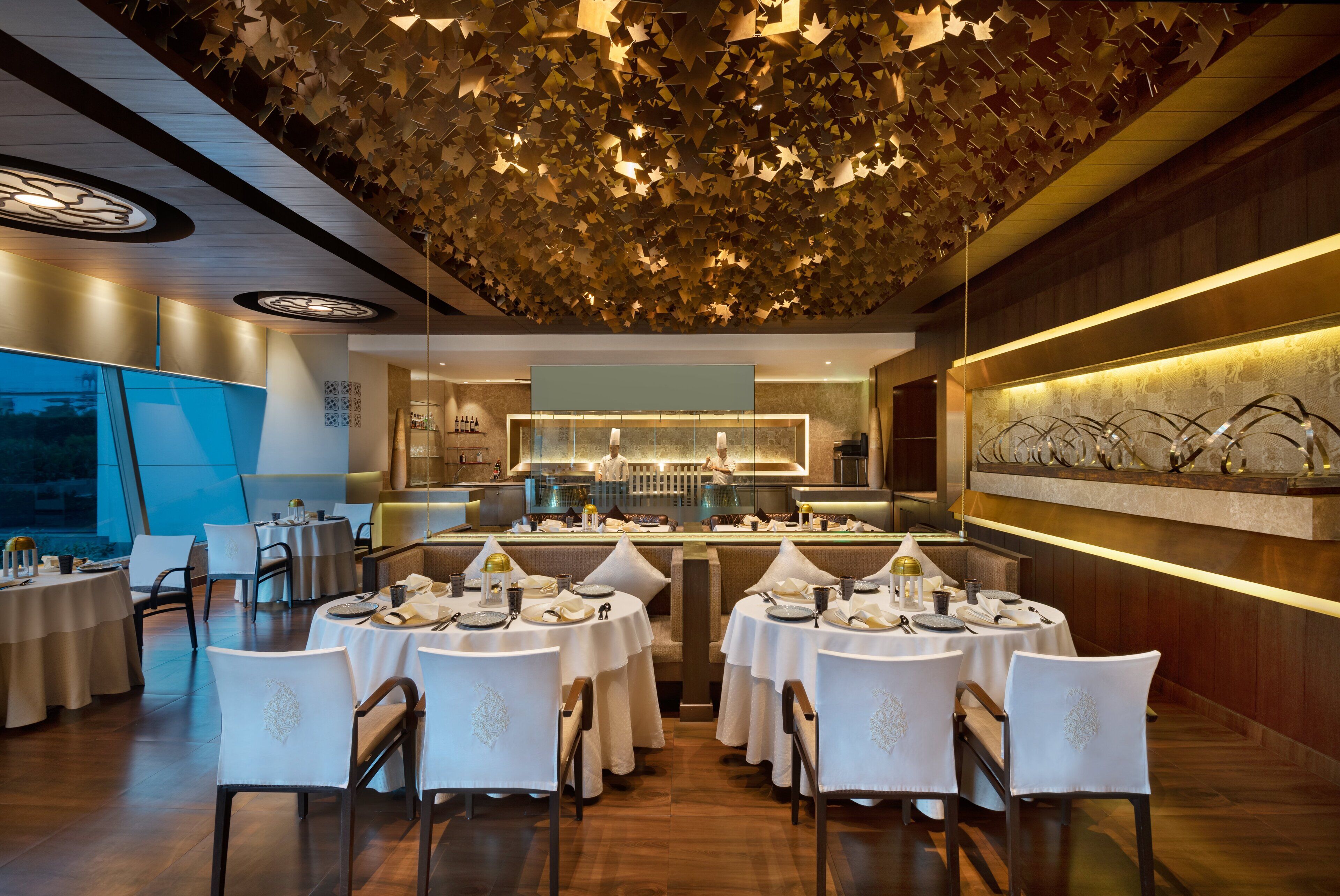 A restaurant with round tables, white chairs, and a ceiling with leaf-like decorations.