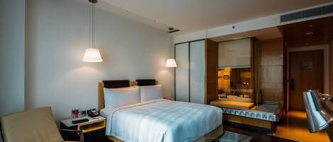 Una habitación de hotel moderna con una cama, una silla, un escritorio, un espejo y zona de ducha.