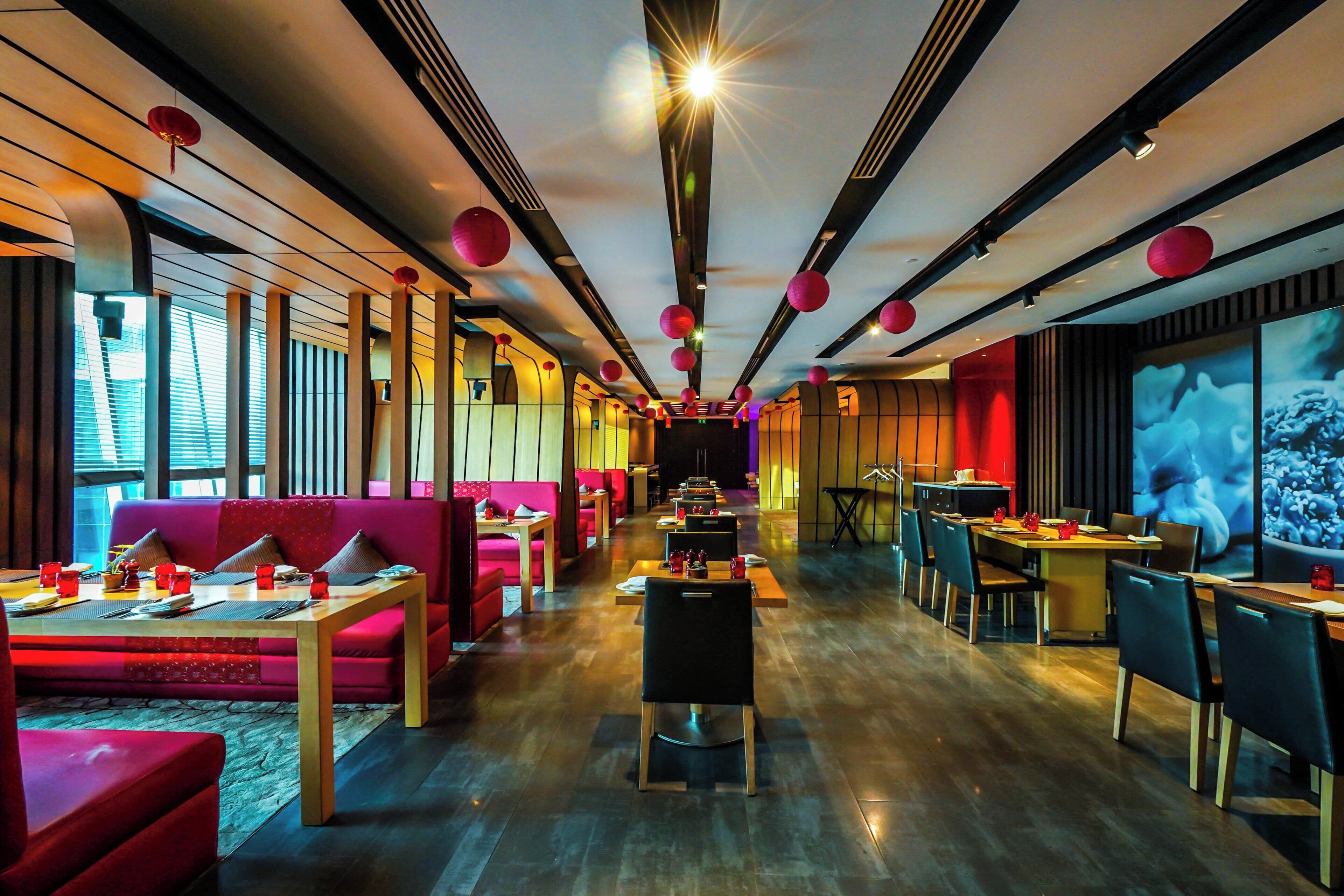 A modern restaurant with red seating, wooden tables, and a central bar area.