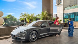 A luxury car parked in front of a building with a large column and a statue.