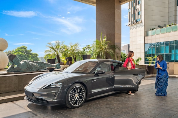 A luxury car parked in front of a building with a large column and a statue.