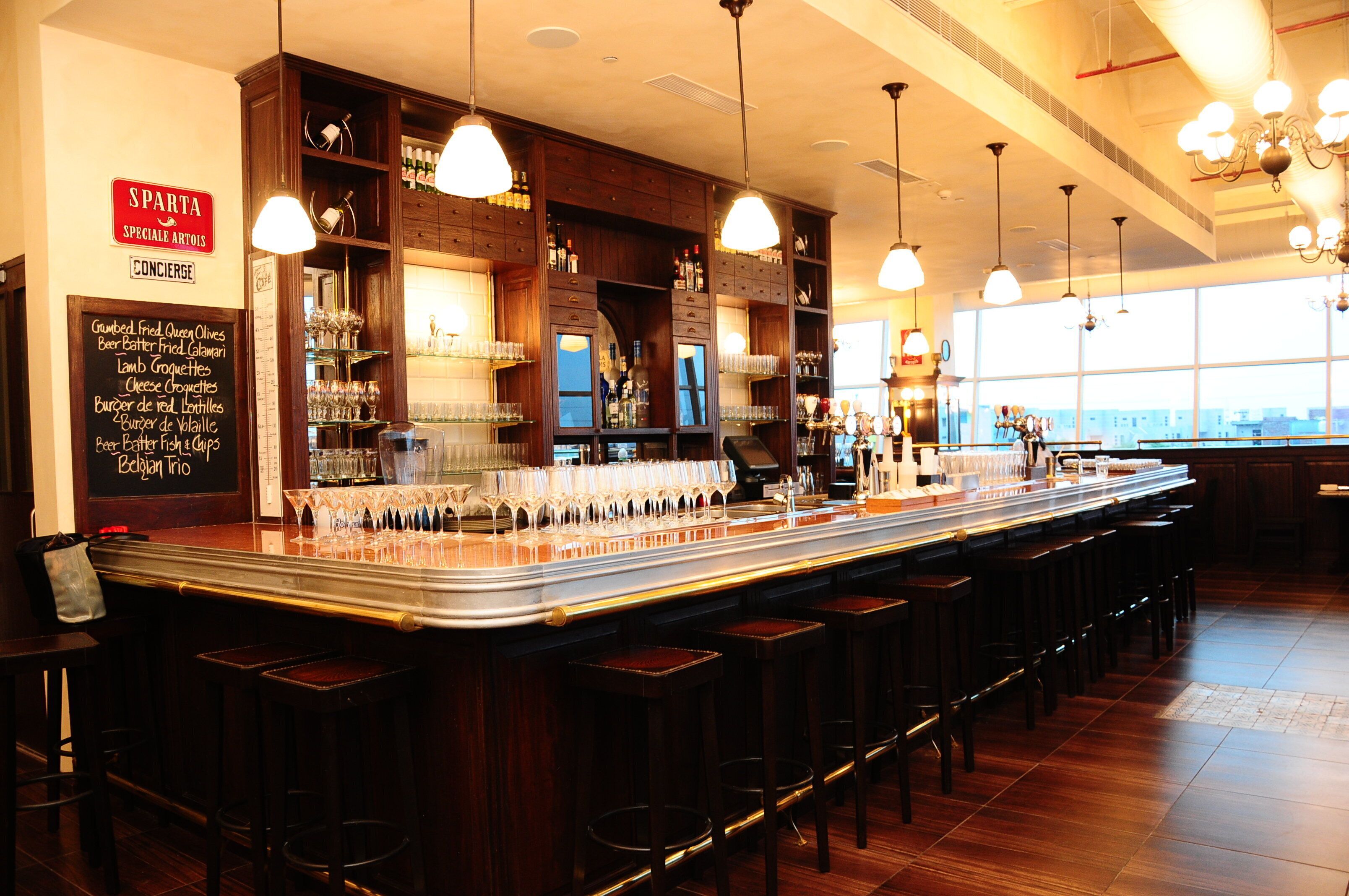 A bar area with a long counter, multiple stools, and a variety of bottles and glasses.