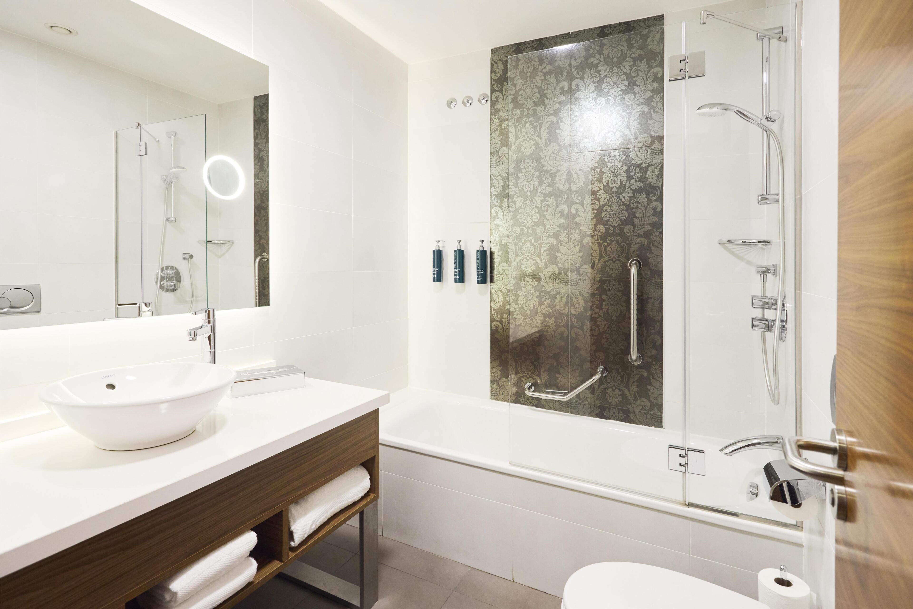 Un bany modern amb dutxa tancada per vidre, un lavabo blanc i un mirall gran.