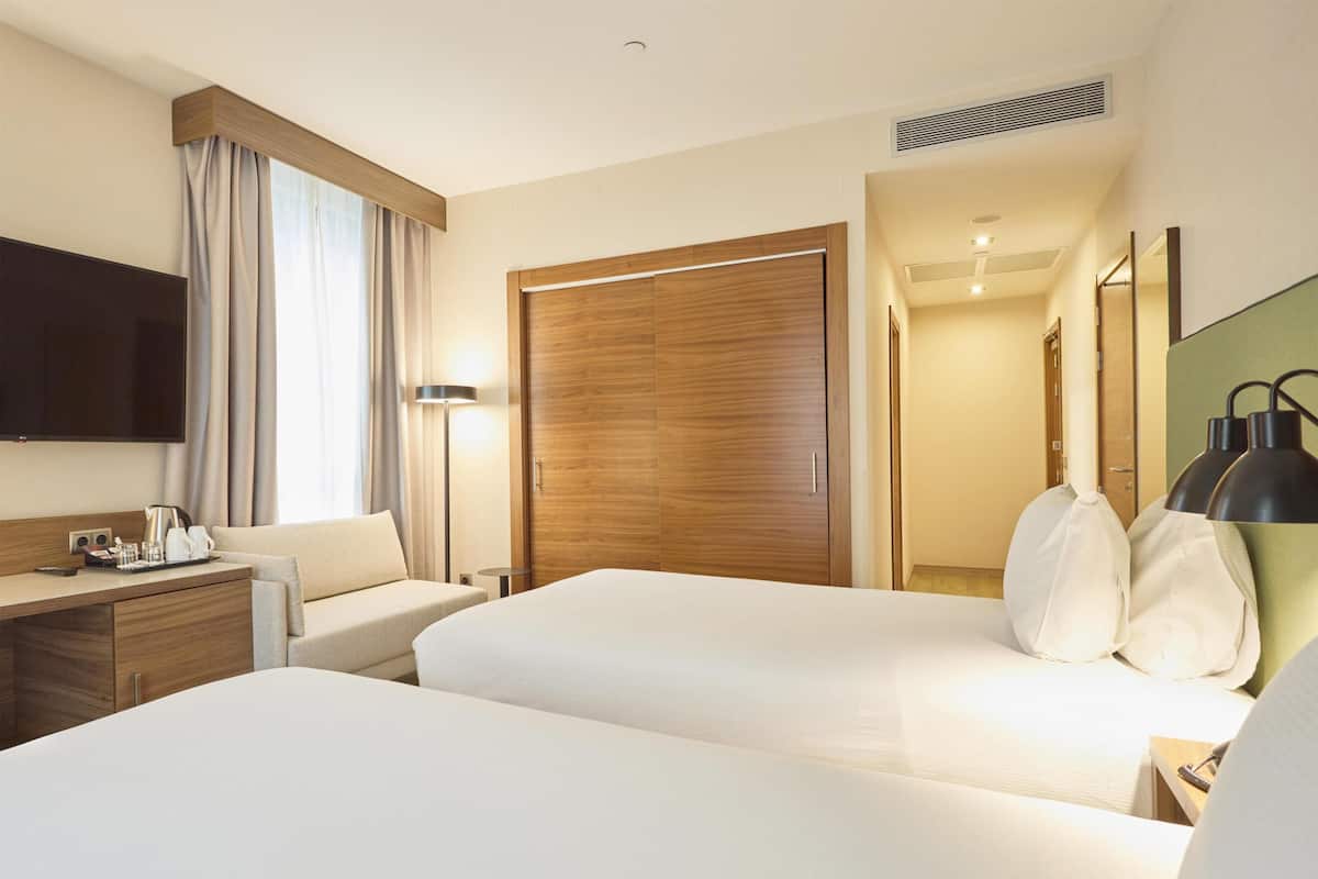 A hotel room with two beds, a desk, a TV, a lamp, and a wardrobe.