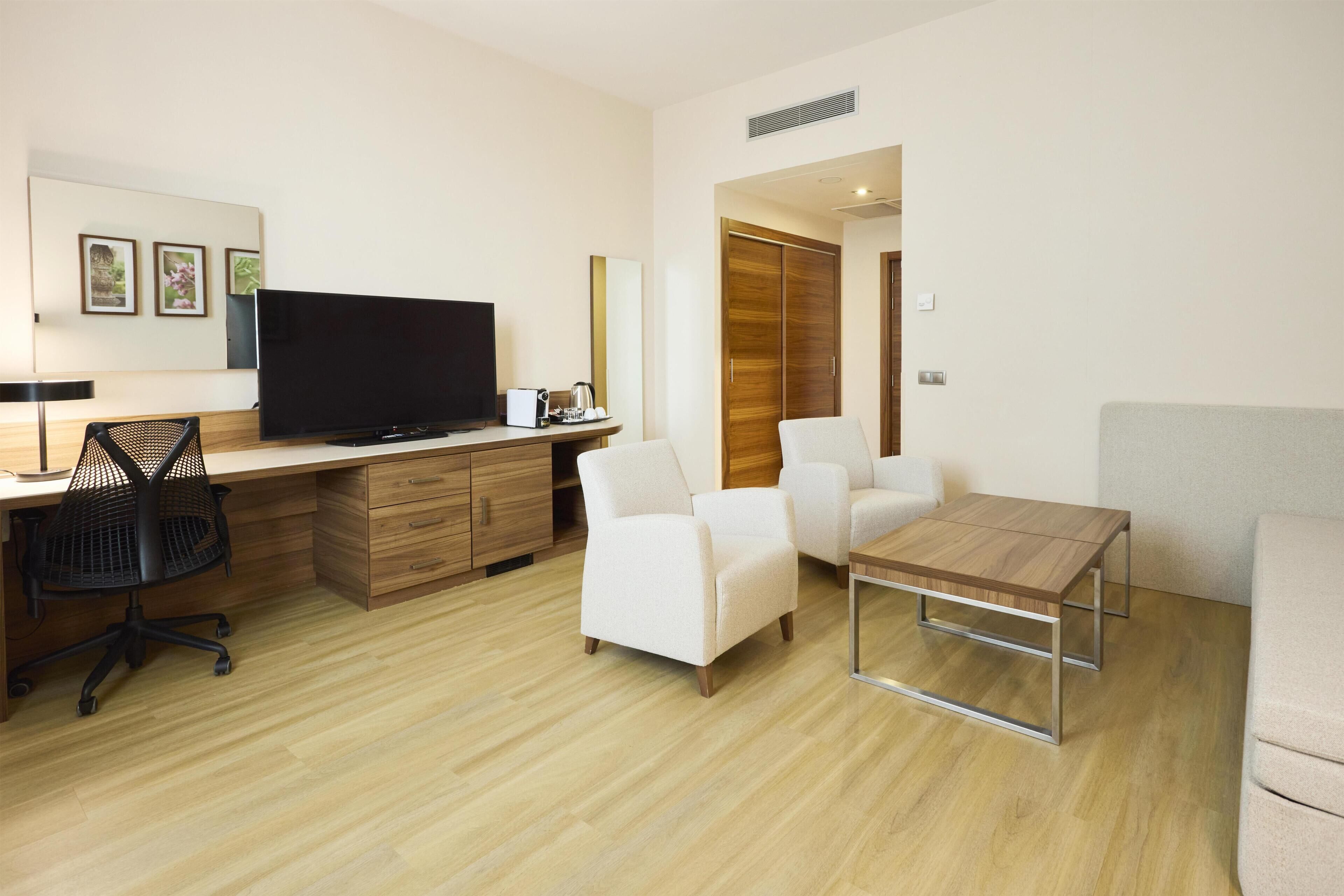 Ein modernes Hotelzimmer mit Flachbildfernseher, einem Holztisch, einer gemütlichen Couch und einem kleinen Couchtisch.