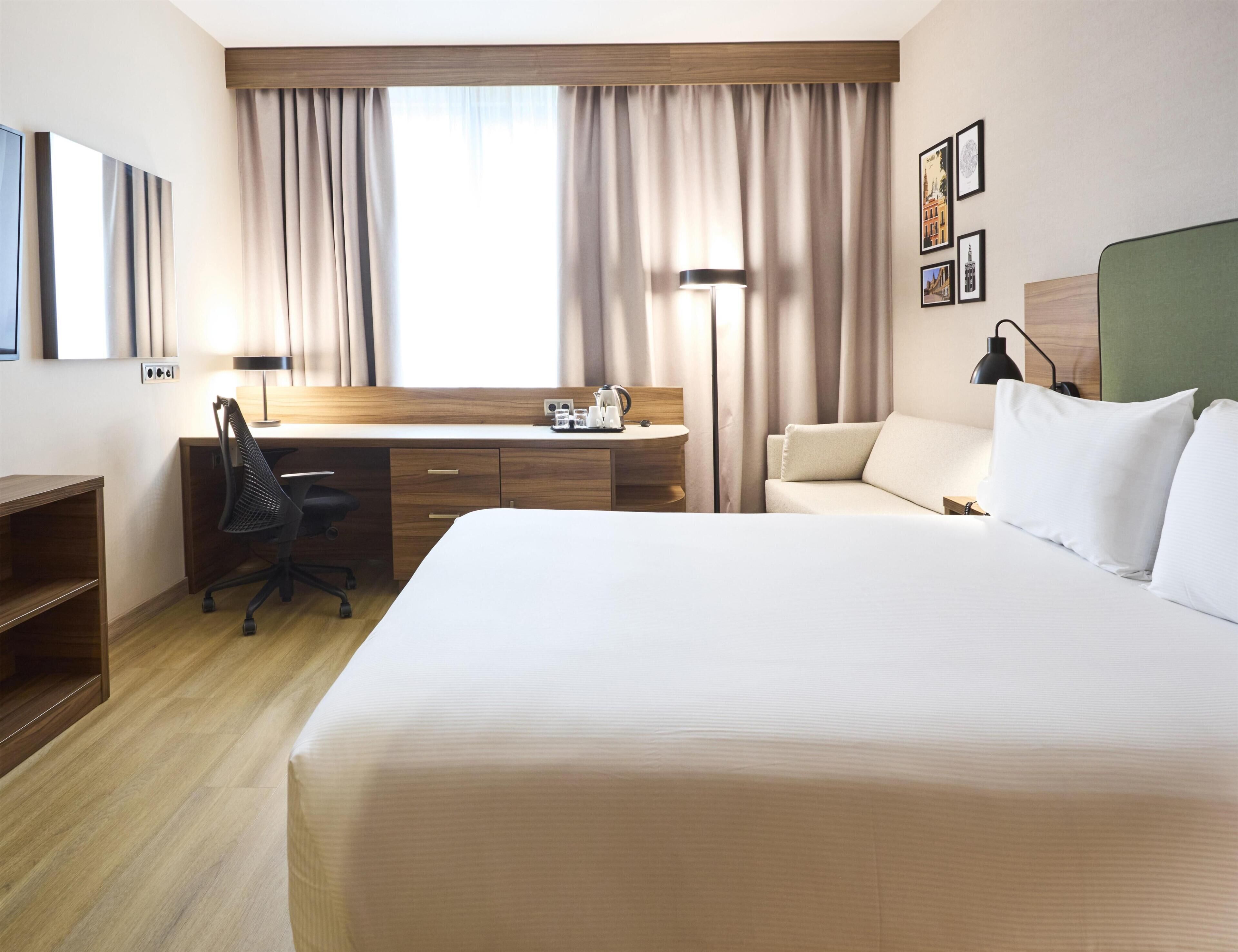 Una habitación de hotel con cama, escritorio, silla y lámpara.