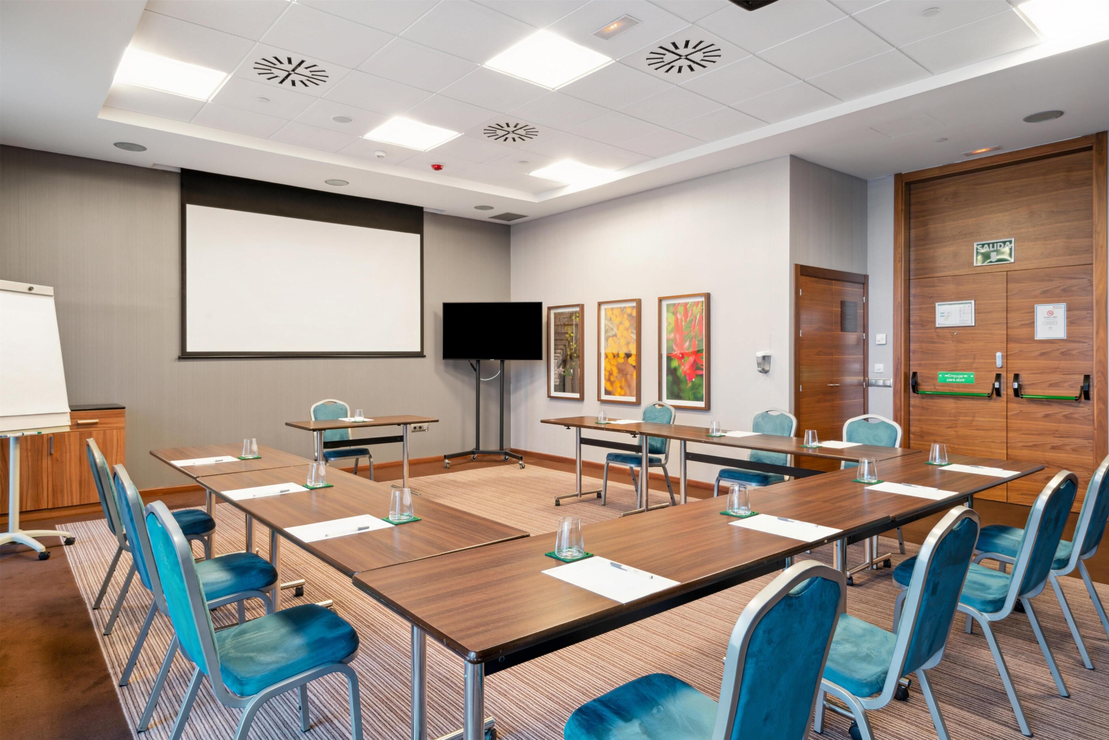 A conference room with a large table, chairs, a projector screen, and artwork on the walls.