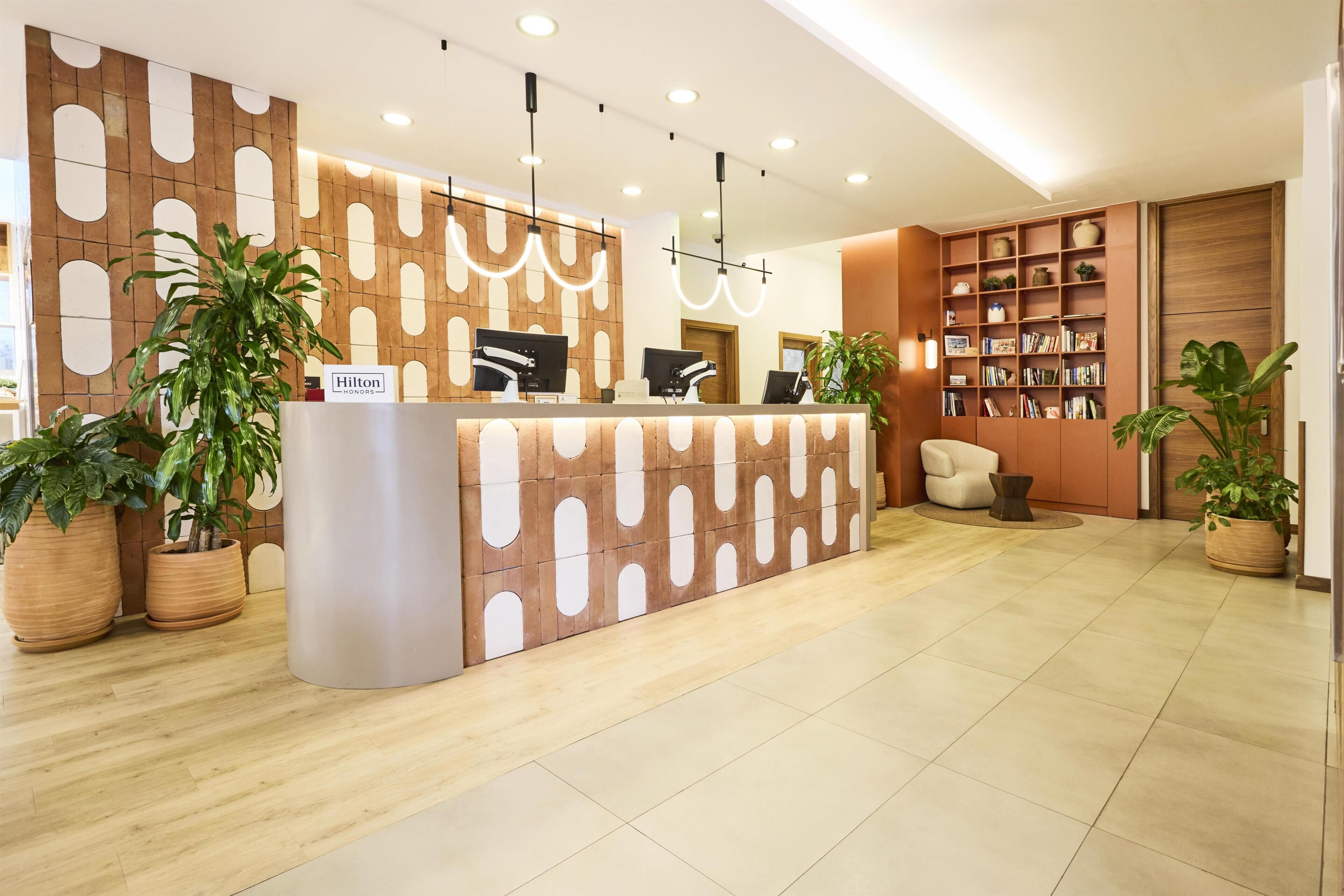 Ein Hotelrezeptionstresen mit modernem Design, eine Sitzecke mit einem Sessel und ein Bücherregal voller Bücher.