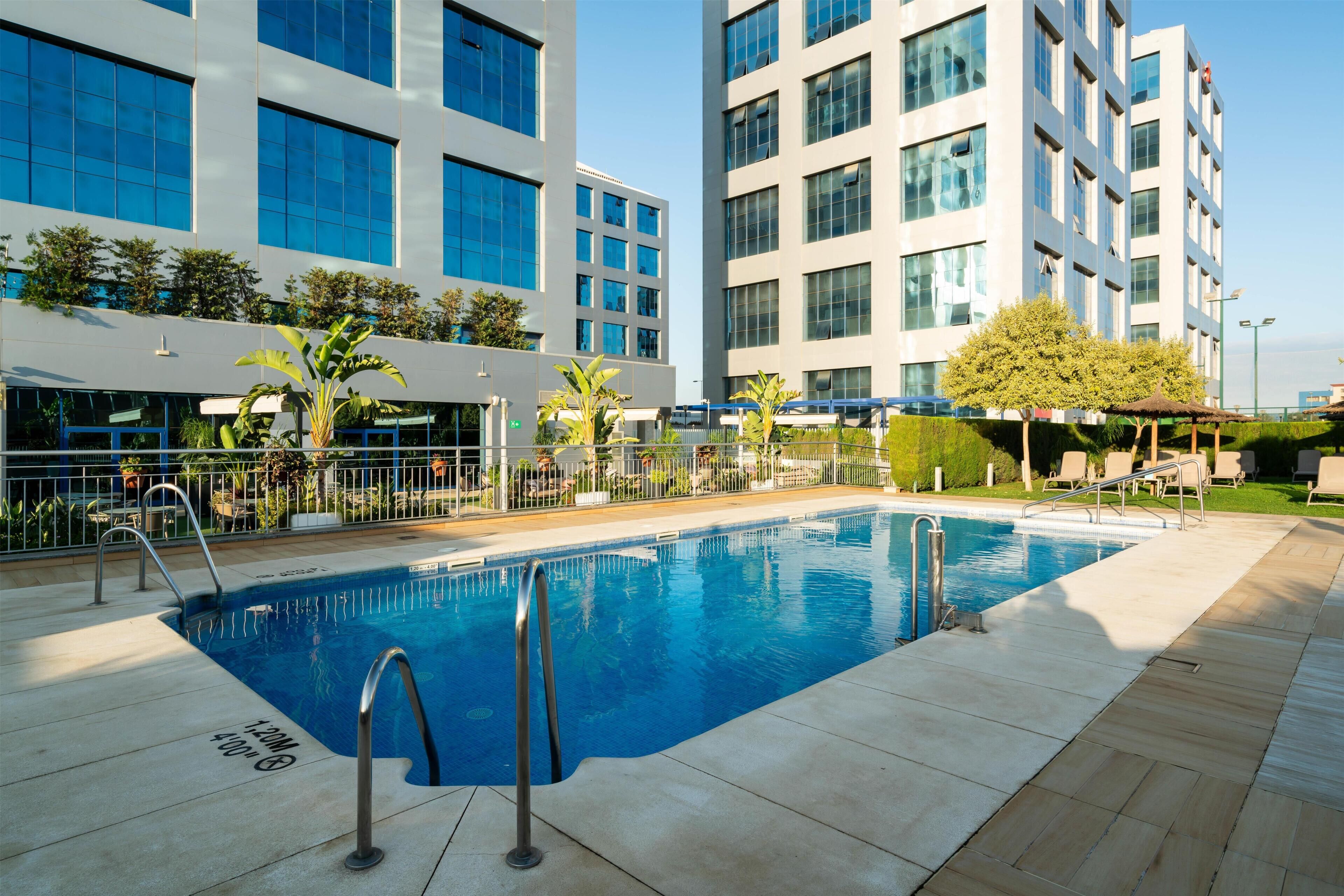 Una piscina con una escalera de metal, rodeada por un patio empedrado.