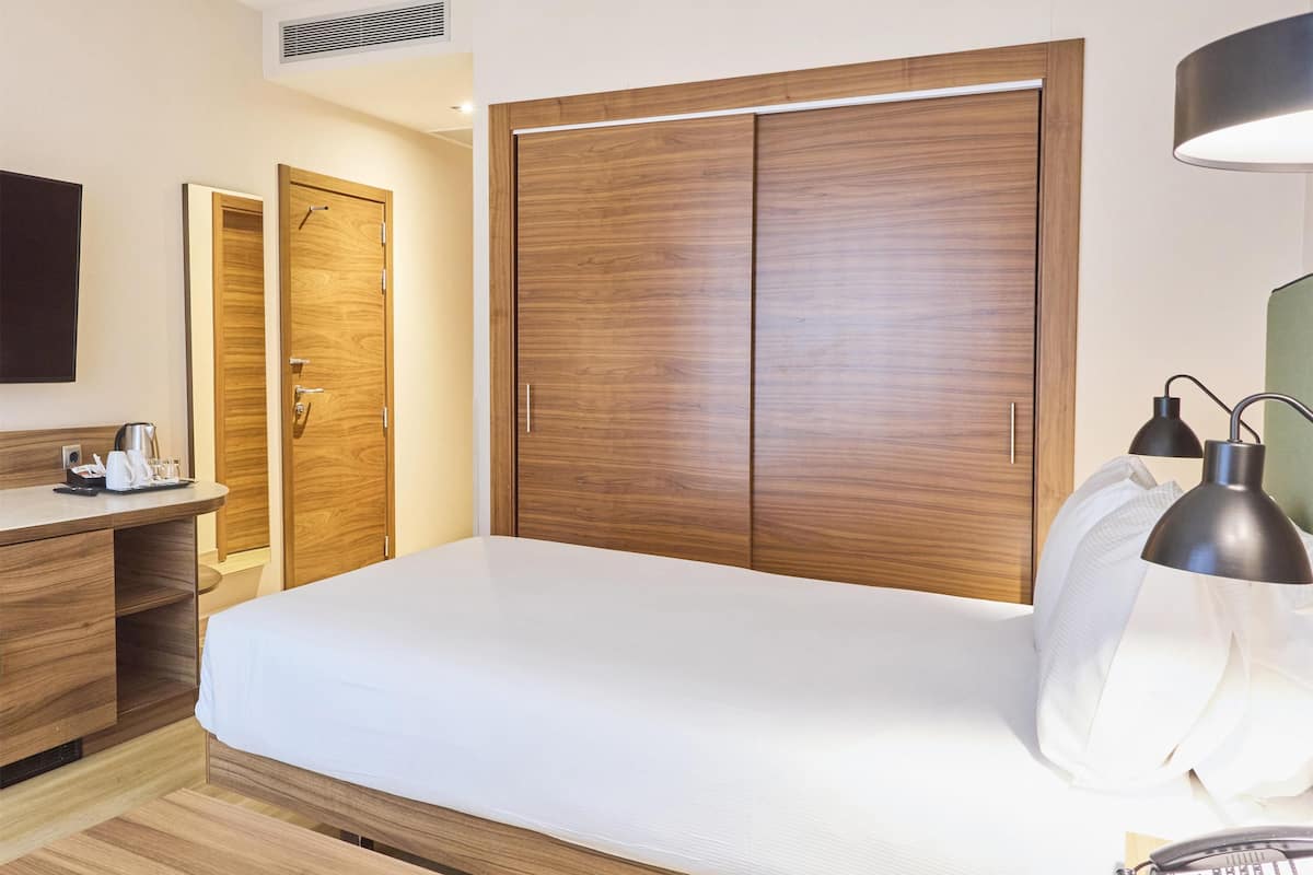 A hotel room with a bed, bedside table, lamp, and a desk with a chair.