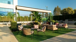 An outdoor seating area with chairs and a sofa, surrounded by potted plants and a building in the background. - Hilton Garden Inn Sevilla (Seville)