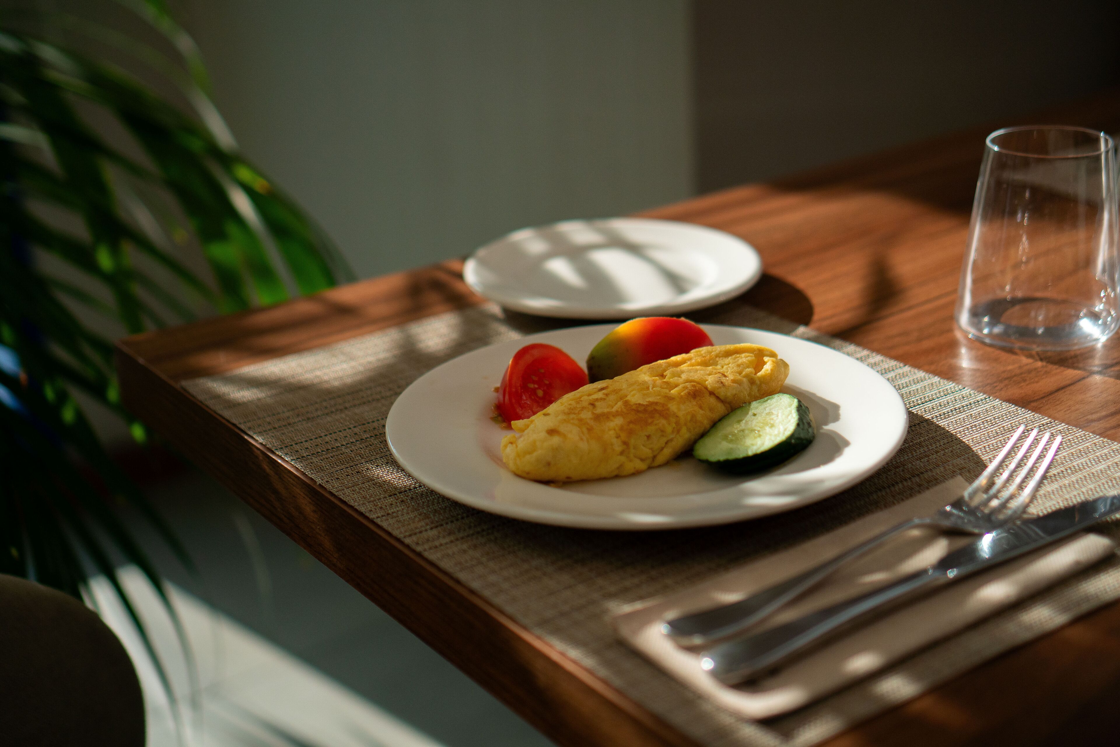 Une table mise pour le petit-déjeuner, avec une assiette de nourriture, un verre et des couverts.