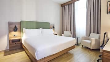 Camera d'hotel con un letto grande, una sedia, una scrivania, una lampada e una finestra con tende.