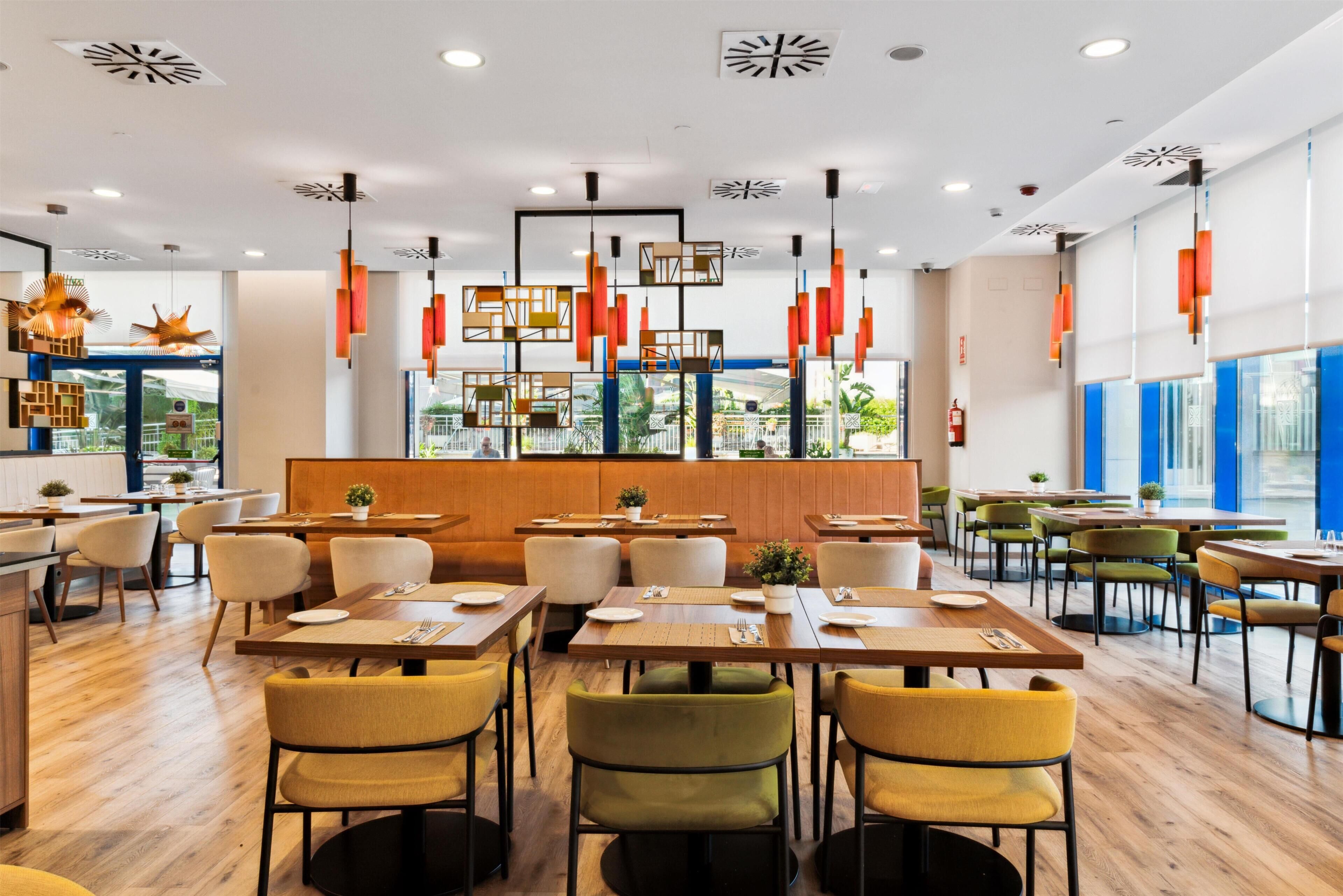 Un intérieur de restaurant moderne avec des tables en bois, des chaises jaunes et des lampes suspendues.