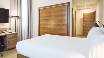 Una habitación de hotel con una cama grande, un armario de madera, escritorio con lámpara y televisión.