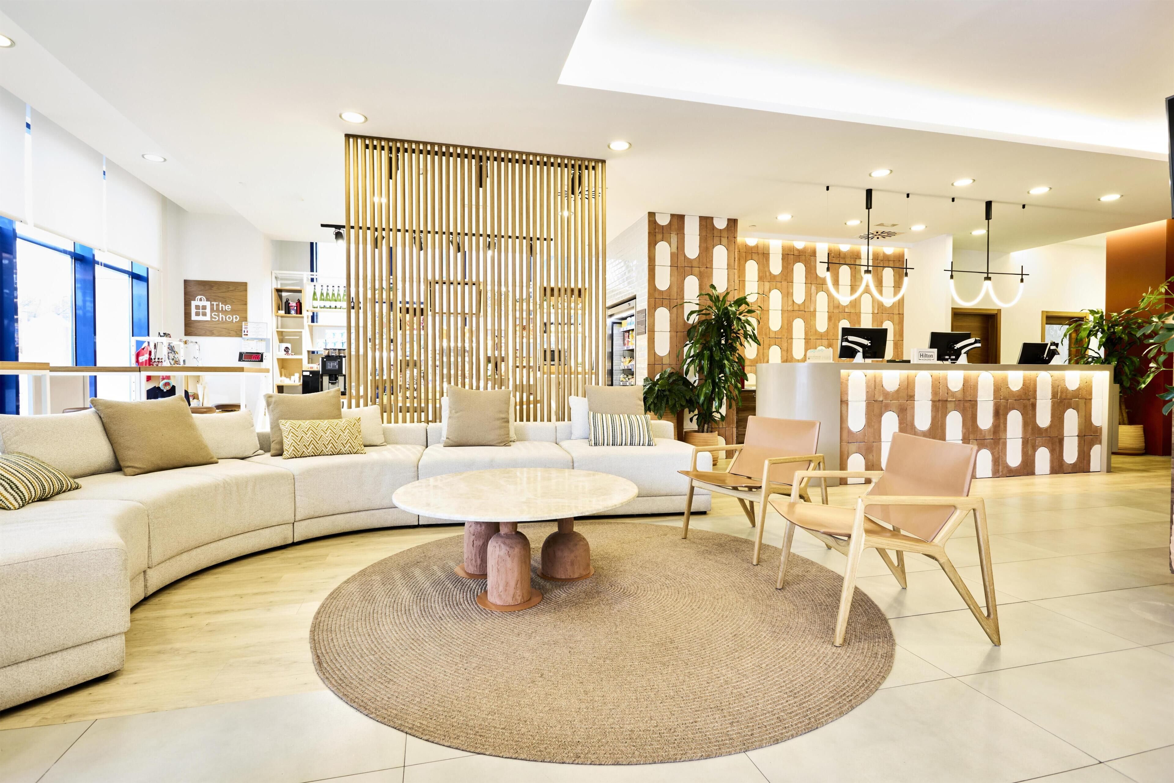 En modern hotellobby med en böjd soffa, ett runt soffbord och en receptionsdisk.