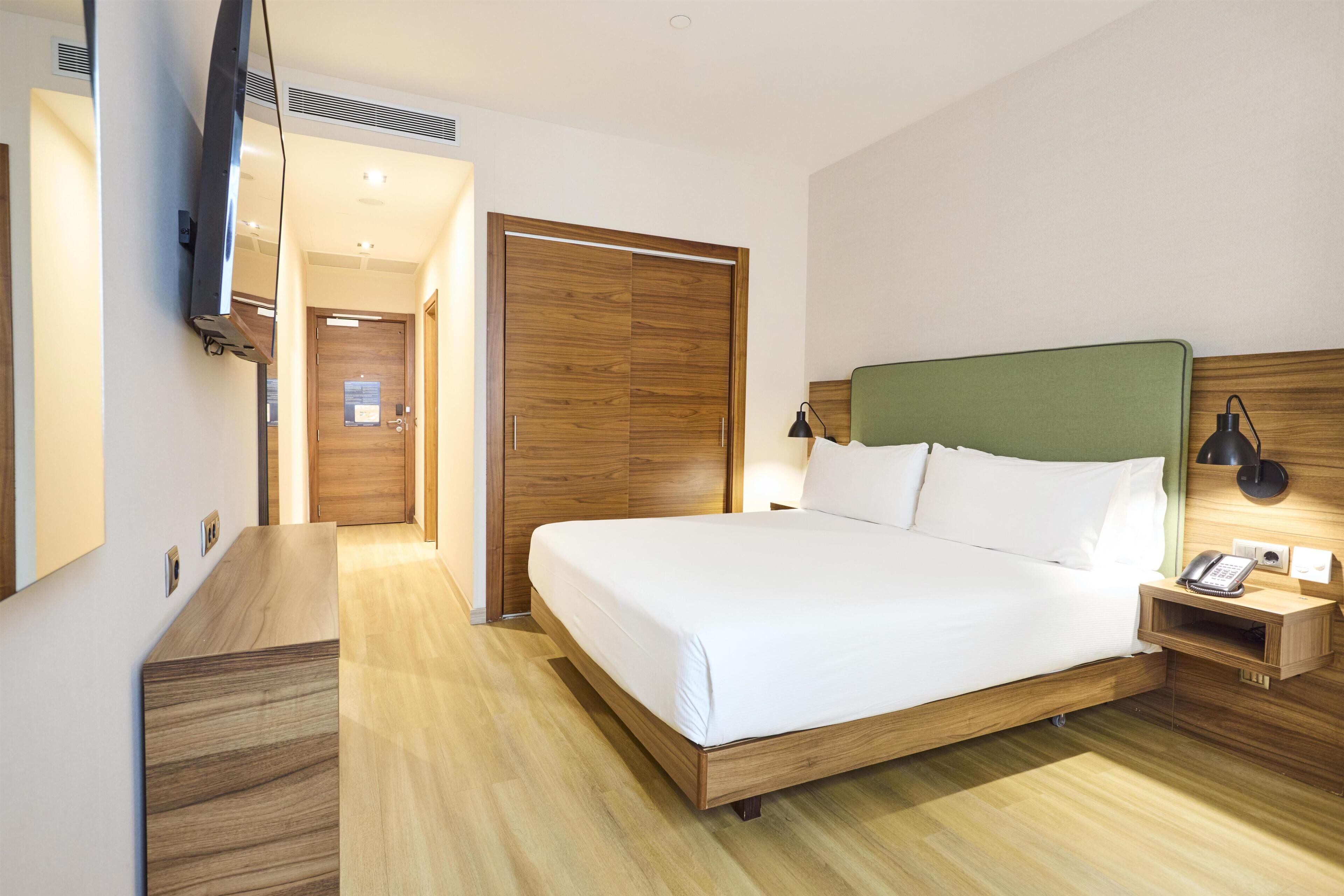 Een hotelkamer met een houten bed, een nachtkastje met een lamp, een telefoon en een spiegel.